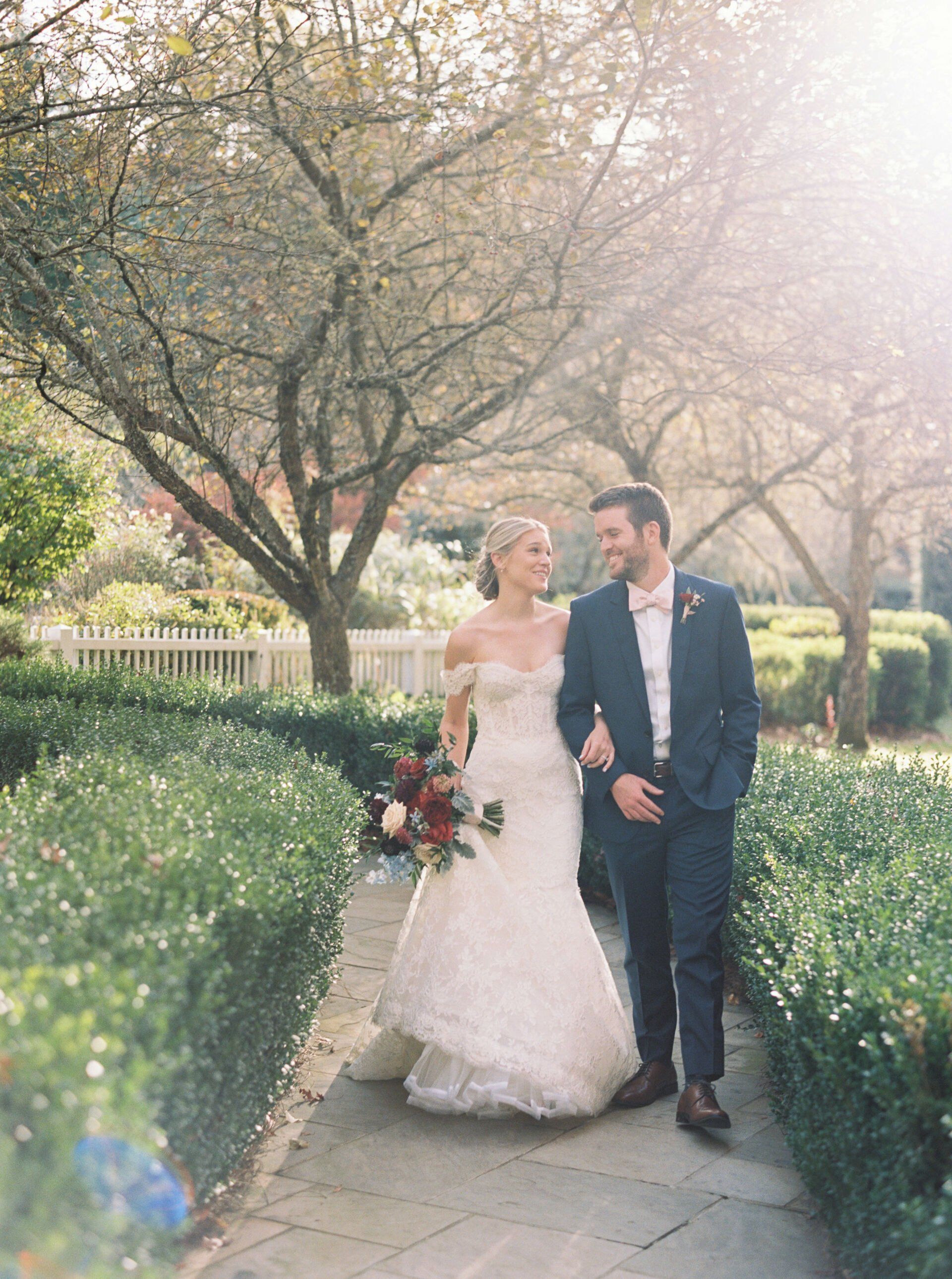 A bride and groom are walking down a path holding hands.