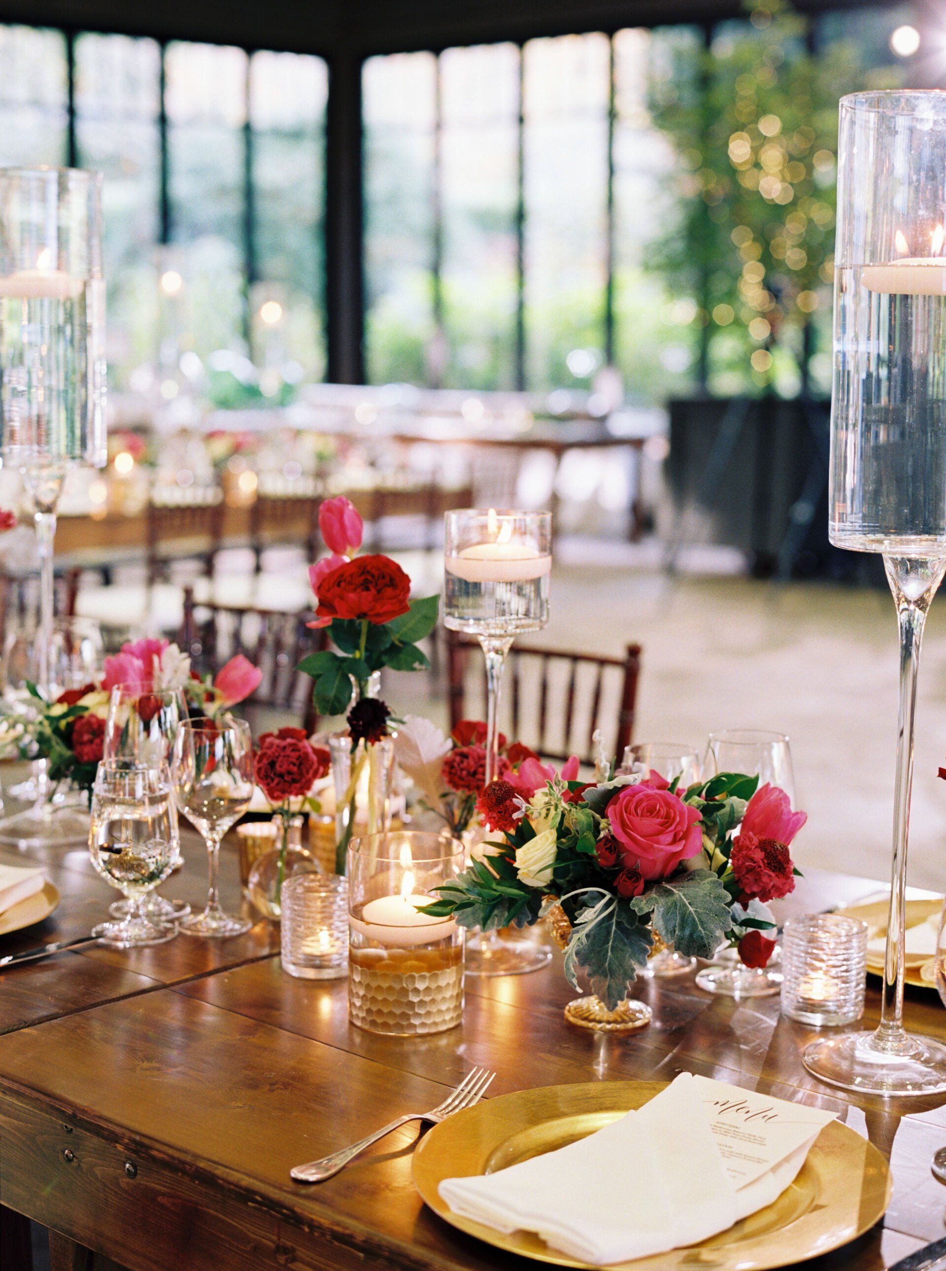 A table set for a wedding reception with plates , candles , and flowers.