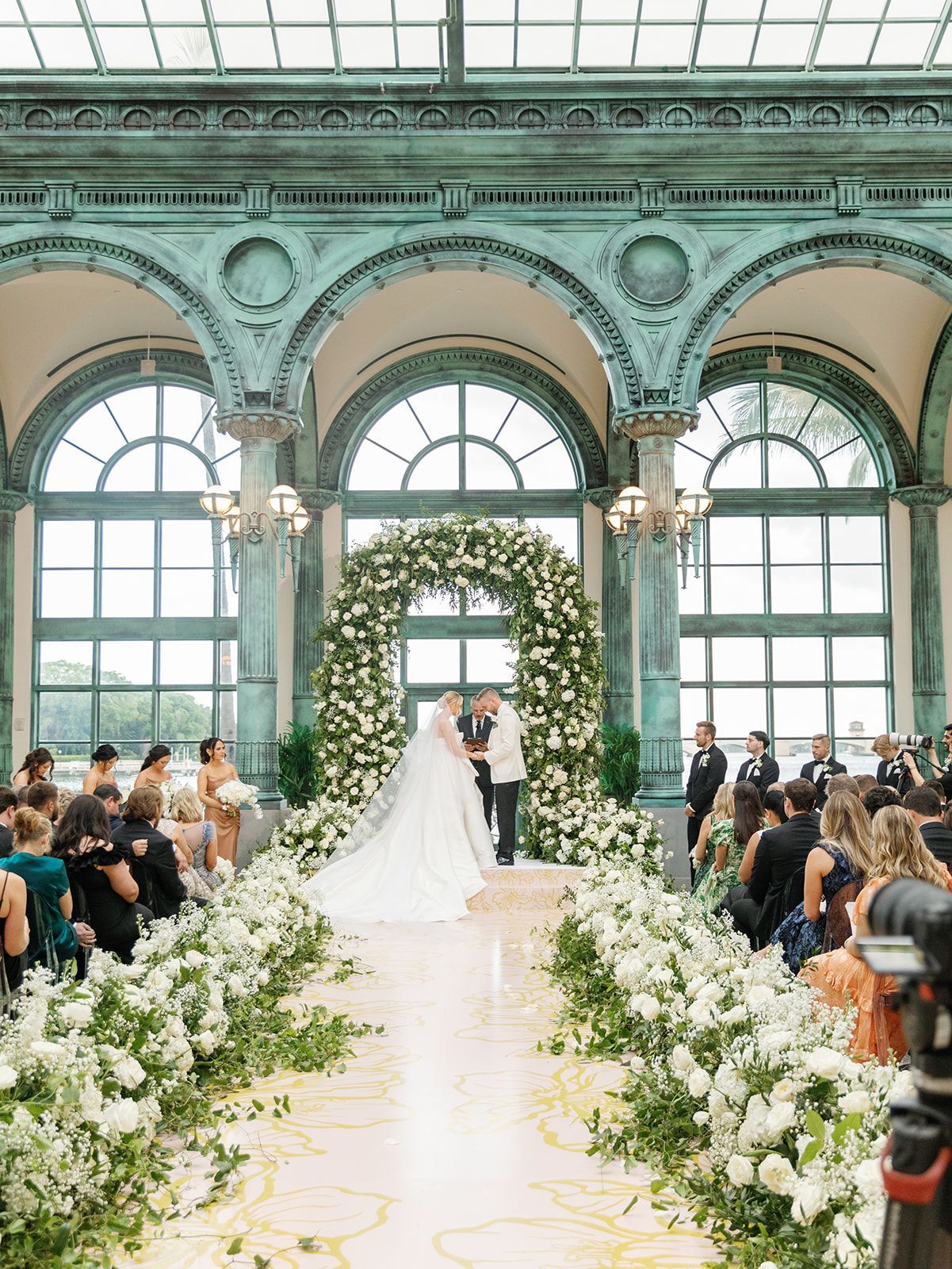 A bride and groom are getting married in a large building surrounded by flowers.