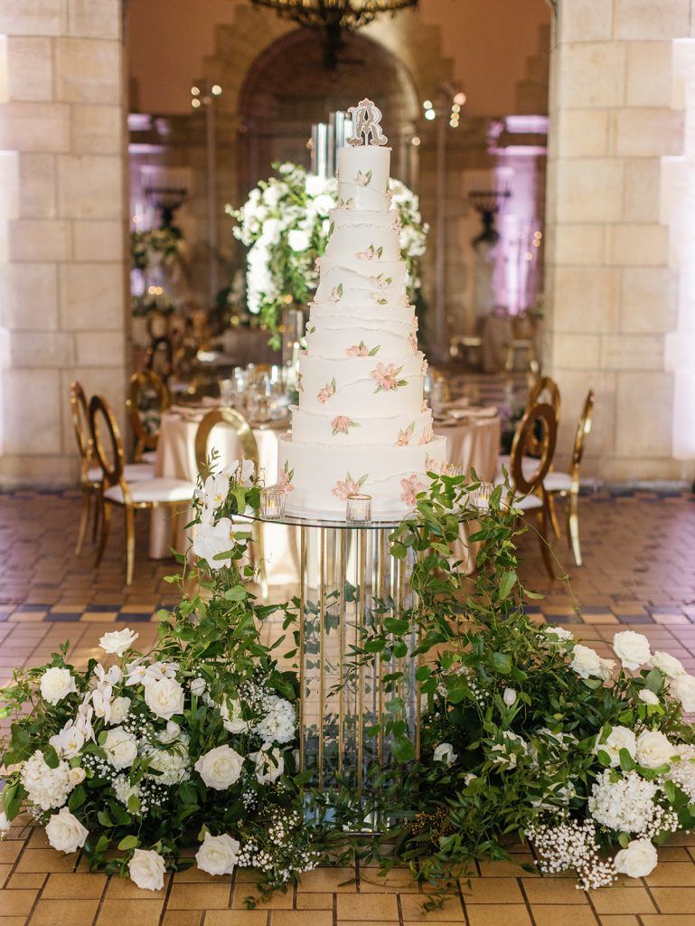A wedding cake is sitting on top of a glass table surrounded by flowers.