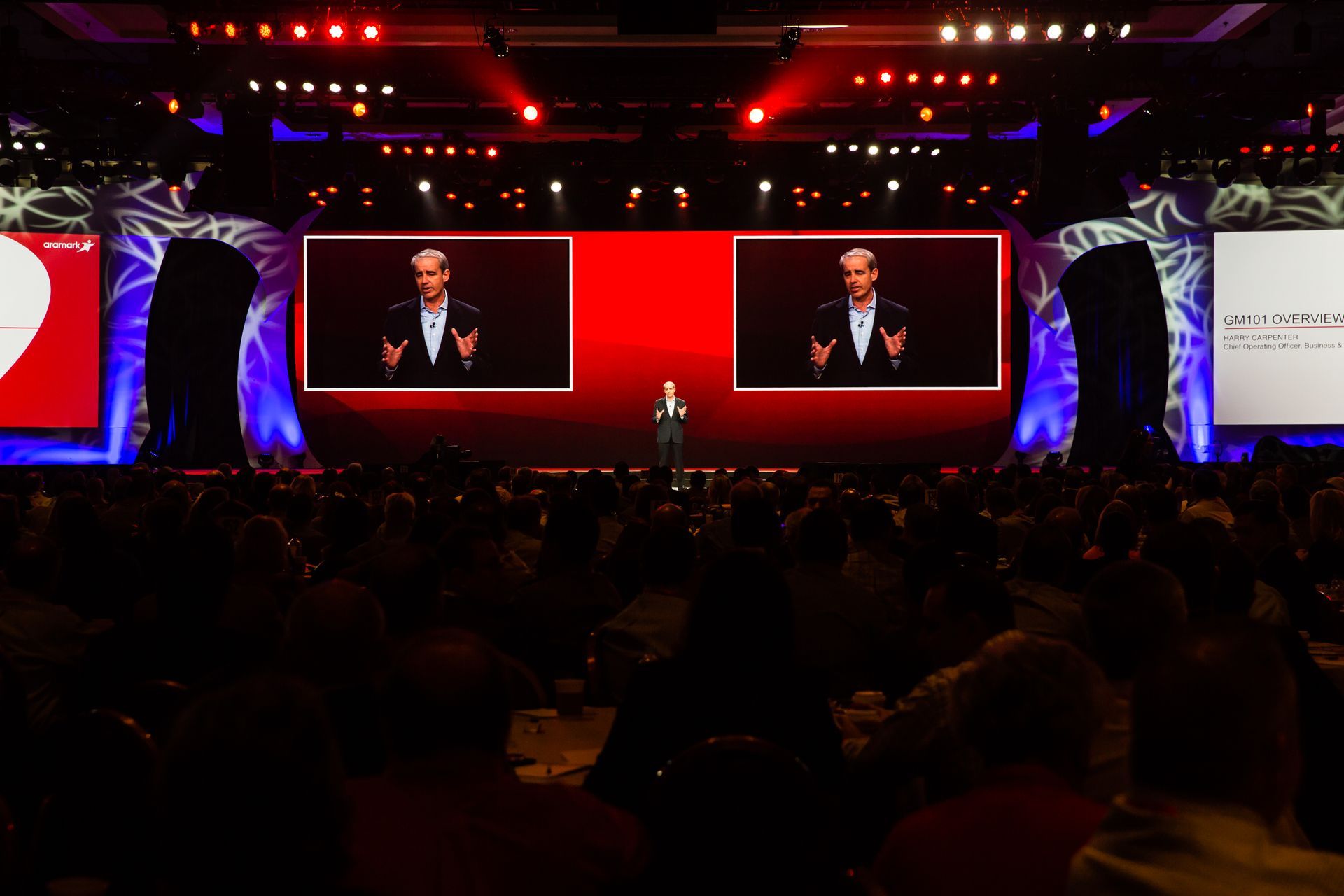 A man is giving a speech on a stage in front of a large crowd.