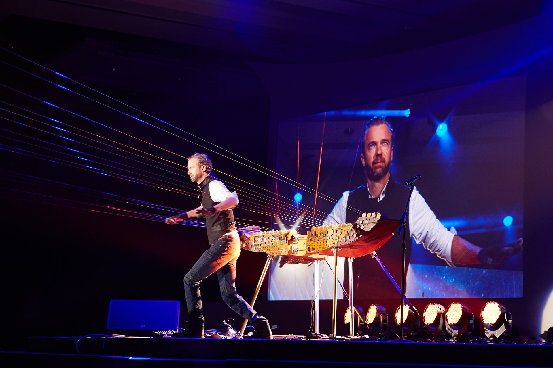 A man is performing a trick on a stage in front of a large screen.