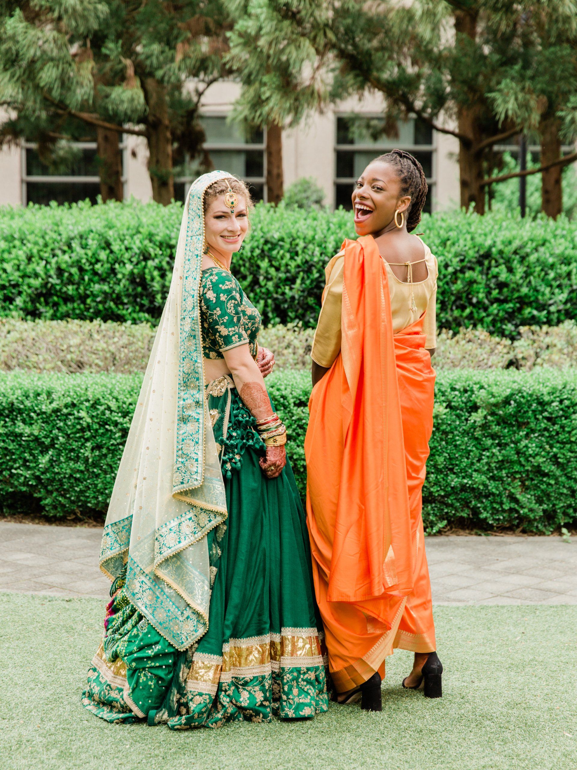 Two women in traditional indian clothing are standing next to each other on a lush green field.