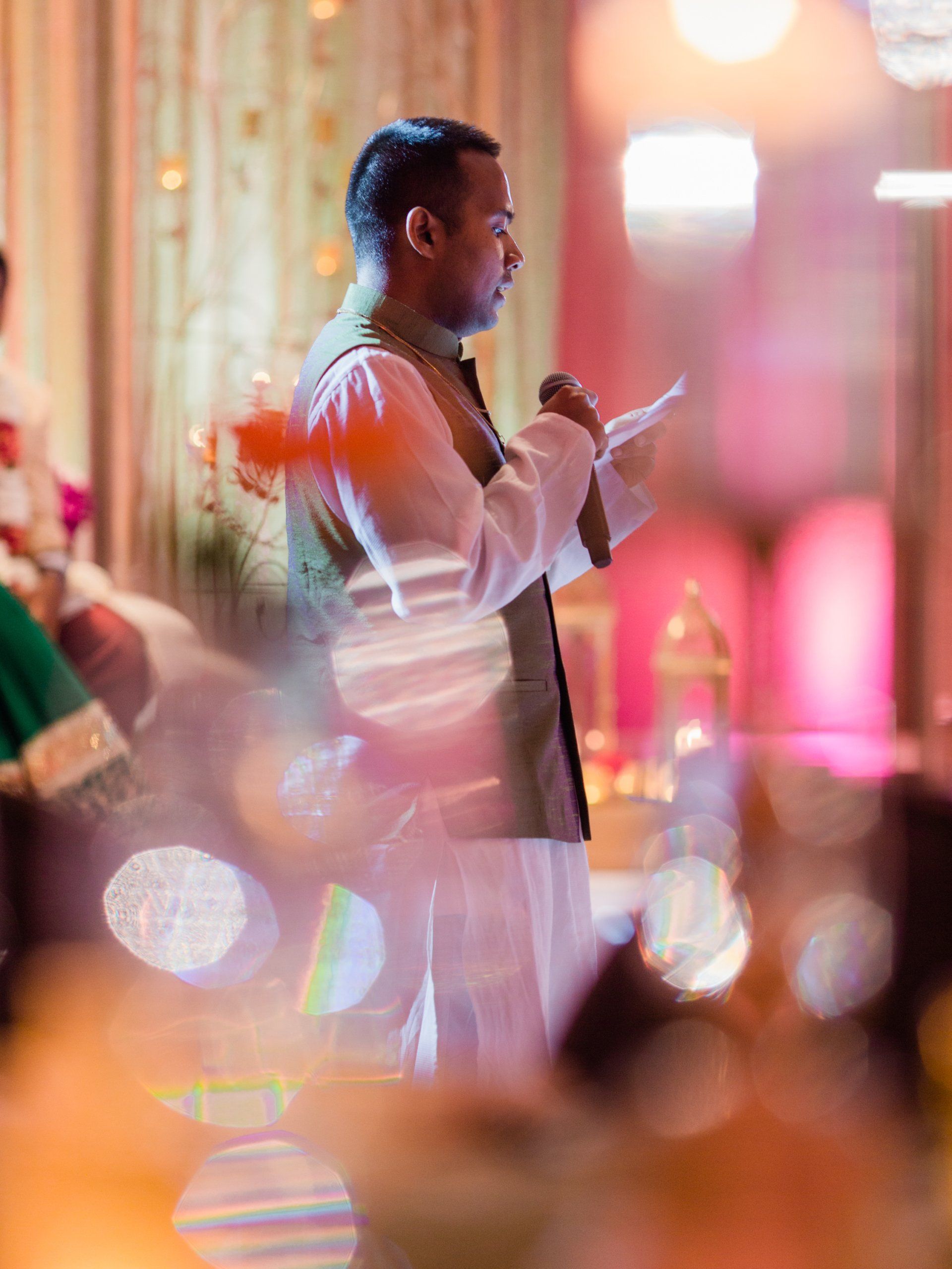A man is holding a microphone and giving a speech at a wedding reception.
