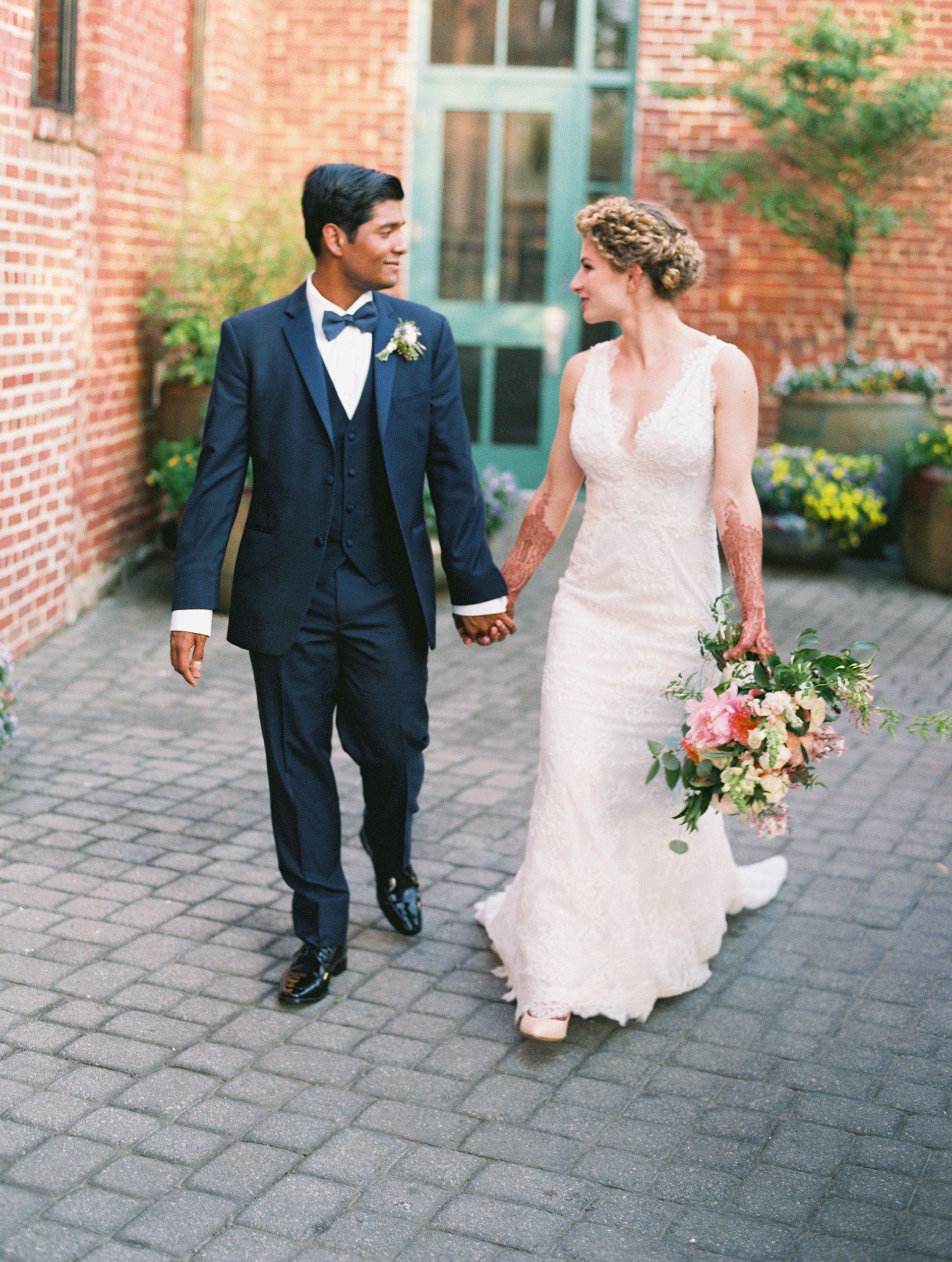 A bride and groom are walking down a brick sidewalk holding hands.