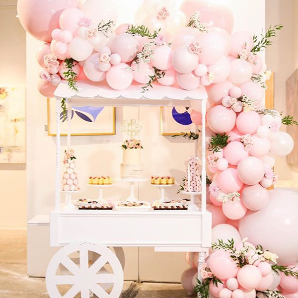 A candy cart decorated with pink balloons and flowers