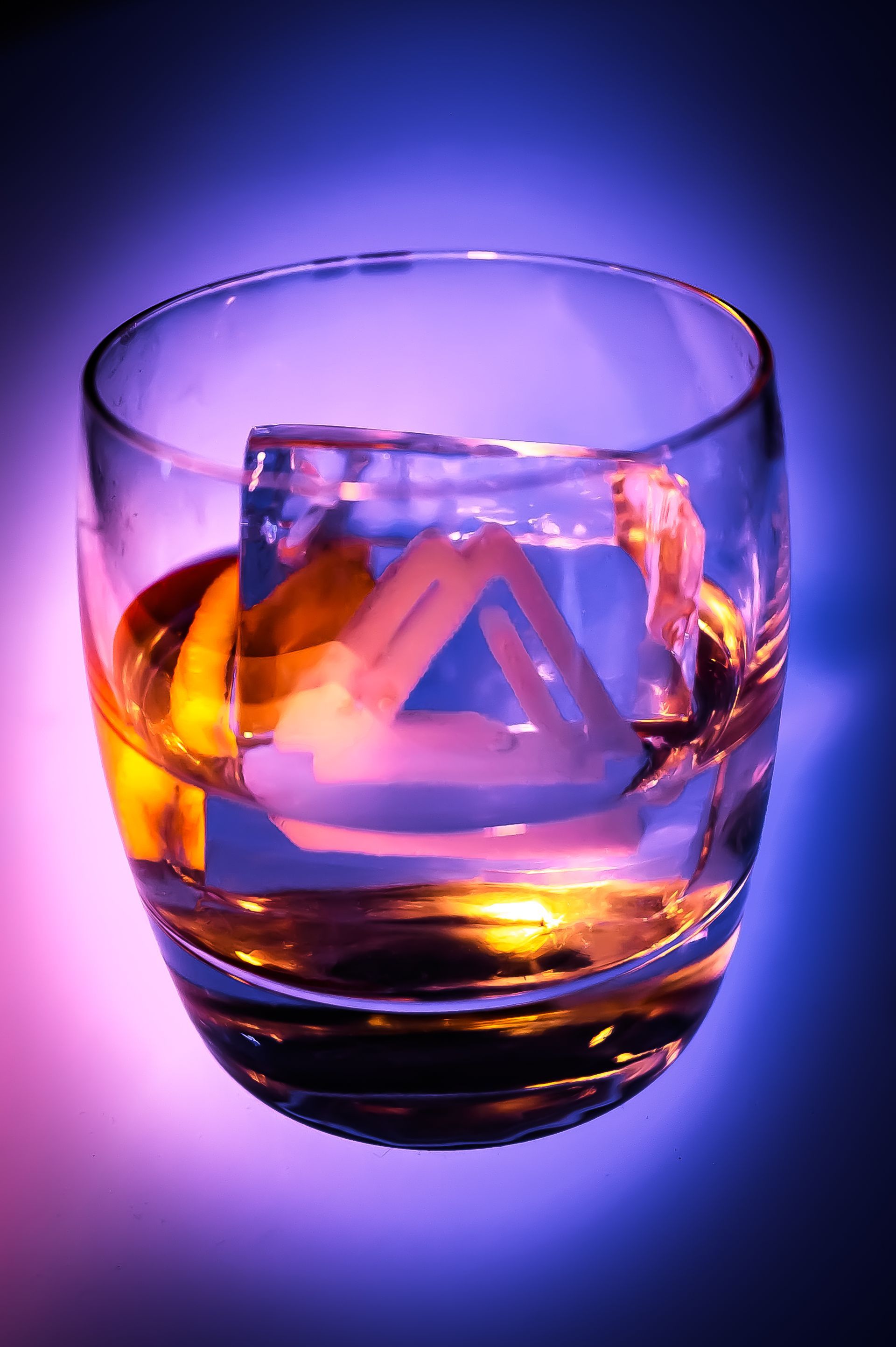 A glass of whiskey with an ice cube in it