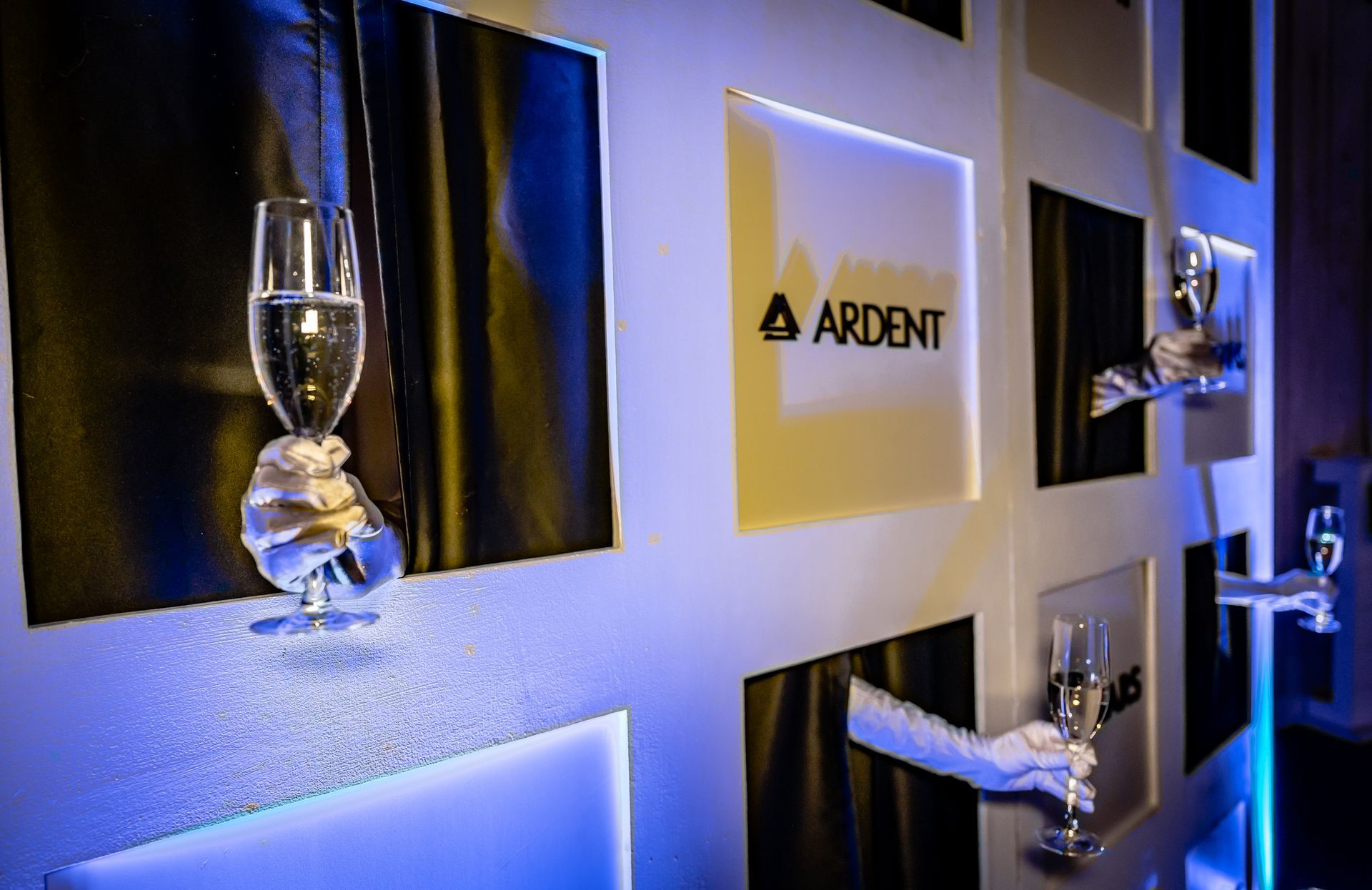 A hand holding a glass of water in front of a sign that says ardent