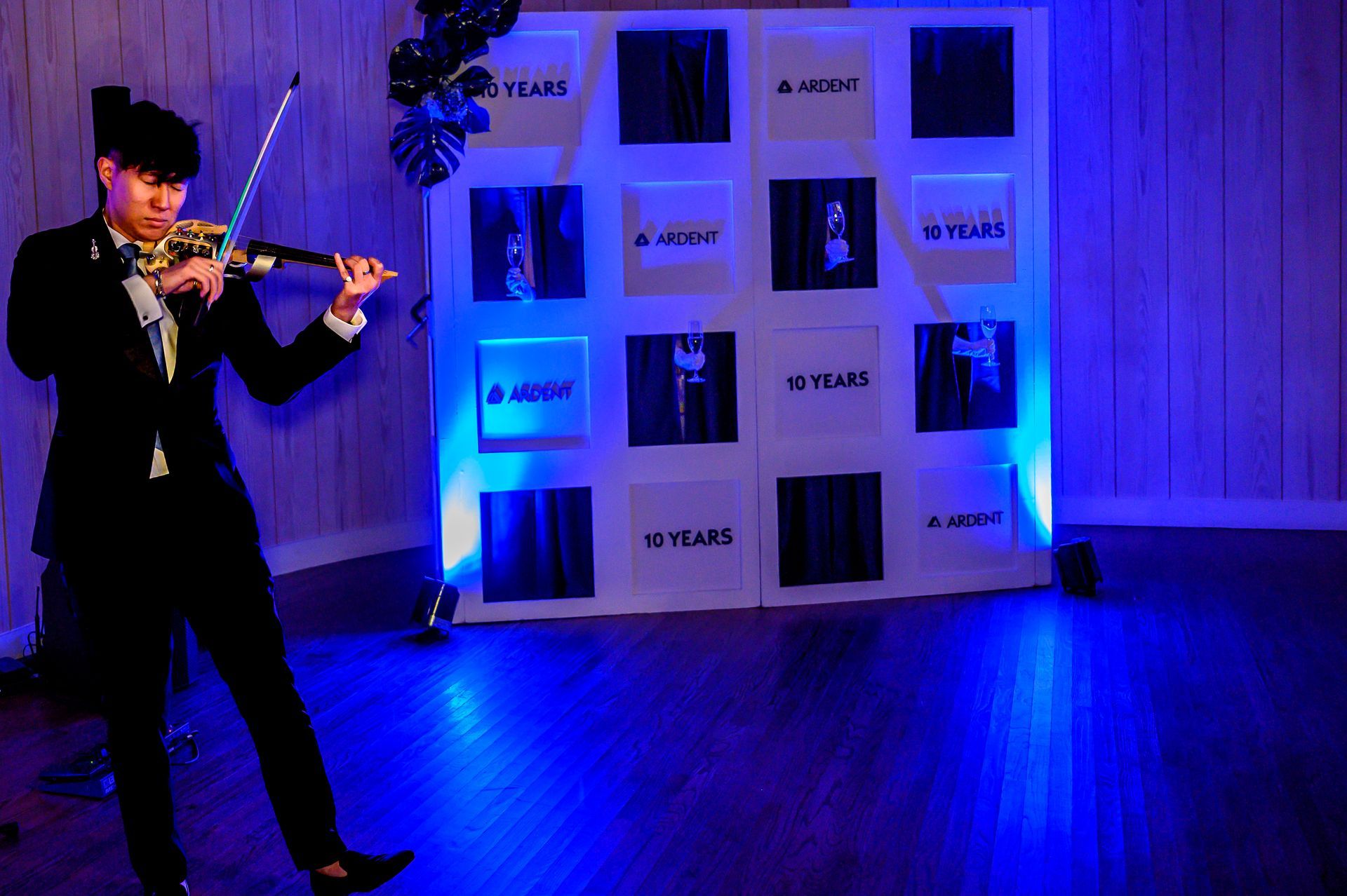 A man in a suit is playing a violin in front of a blue wall.