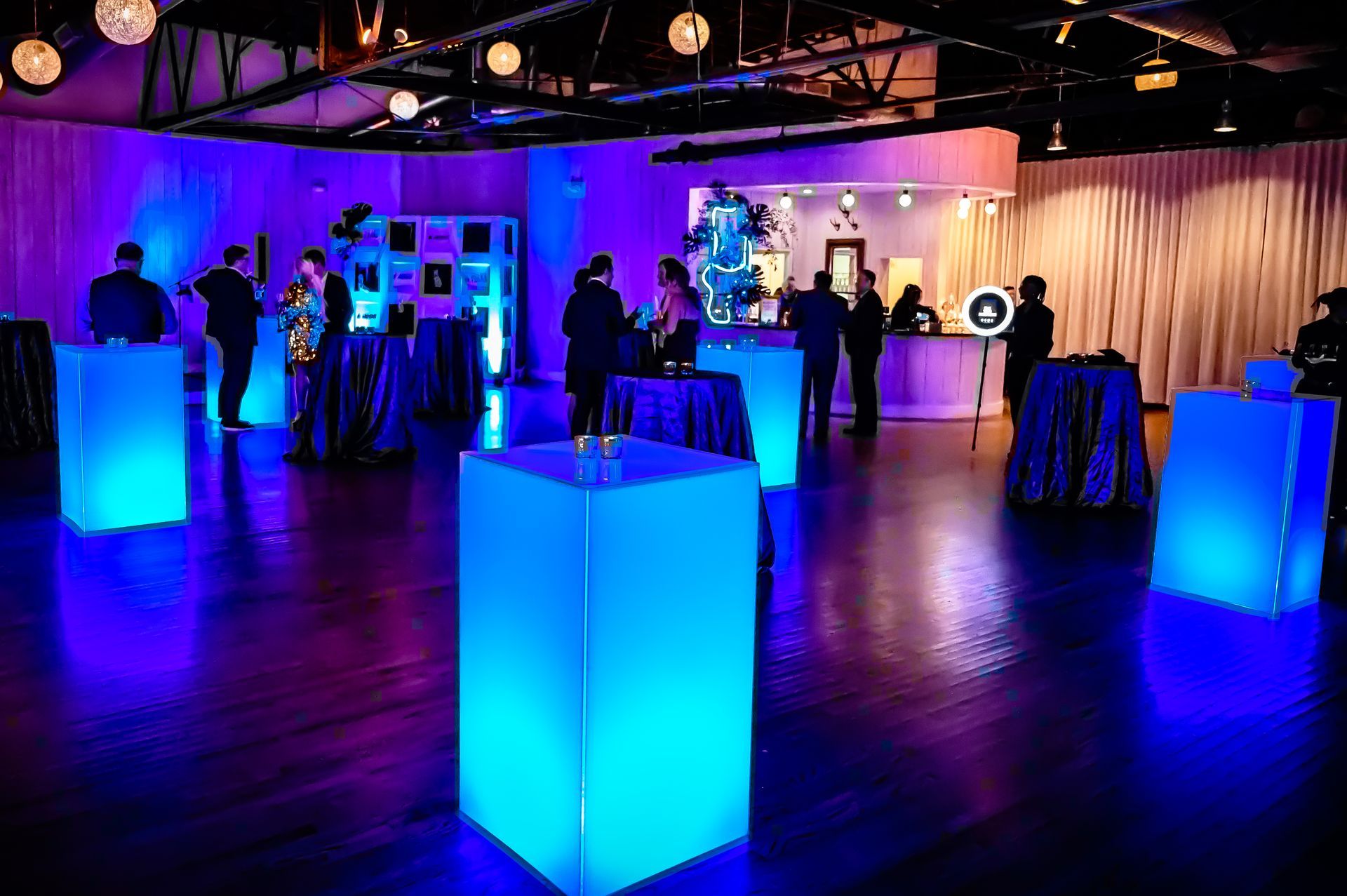 A group of people are standing around tables in a room with blue lights.