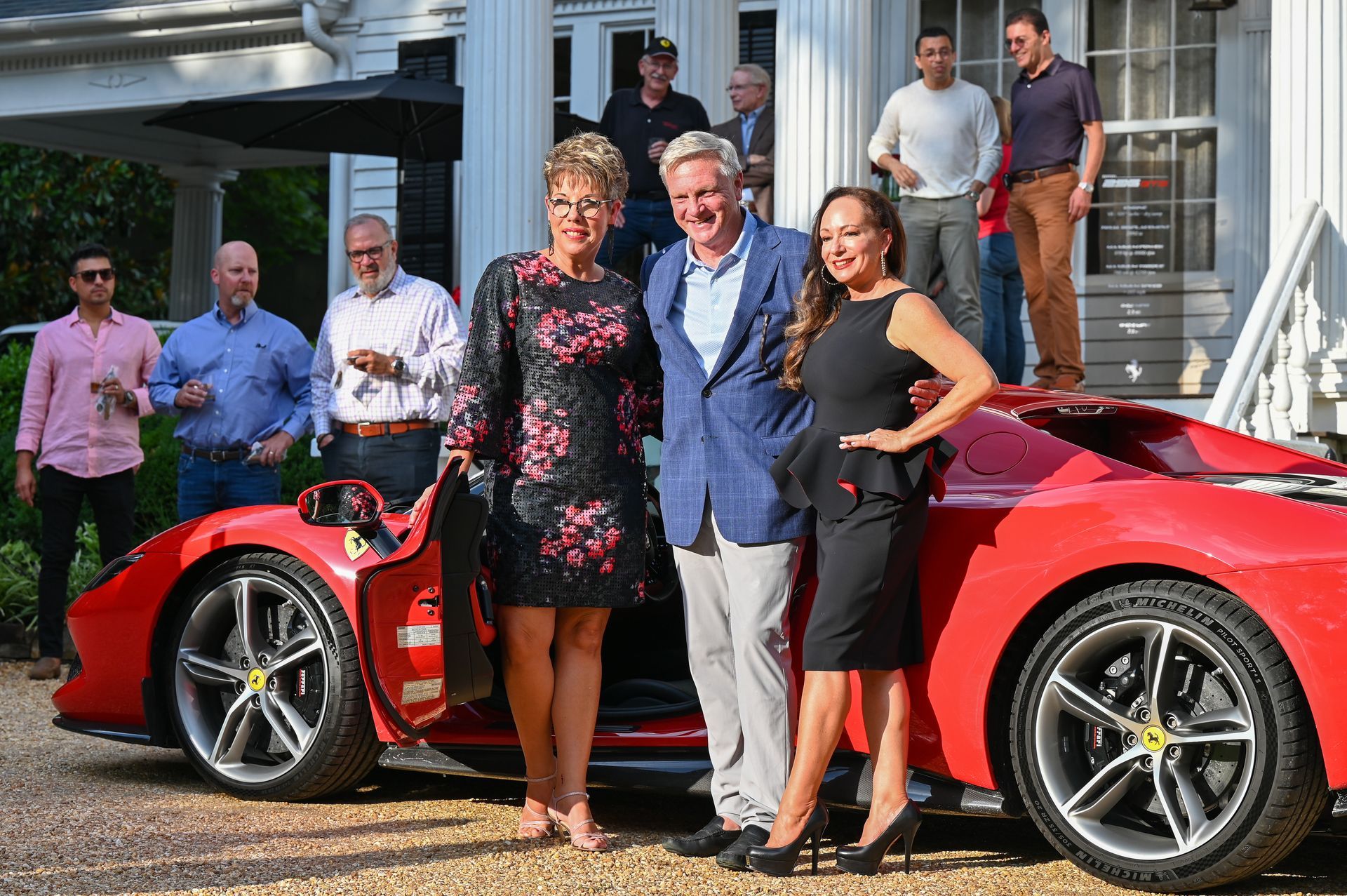 A group of people are standing in front of a red sports car.