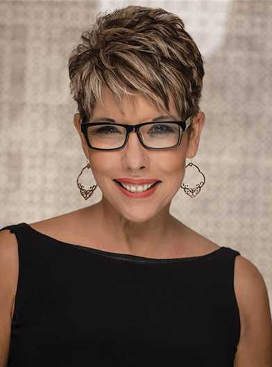 Smiling woman with short highlighted hair, glasses, and heart earrings against a neutral background