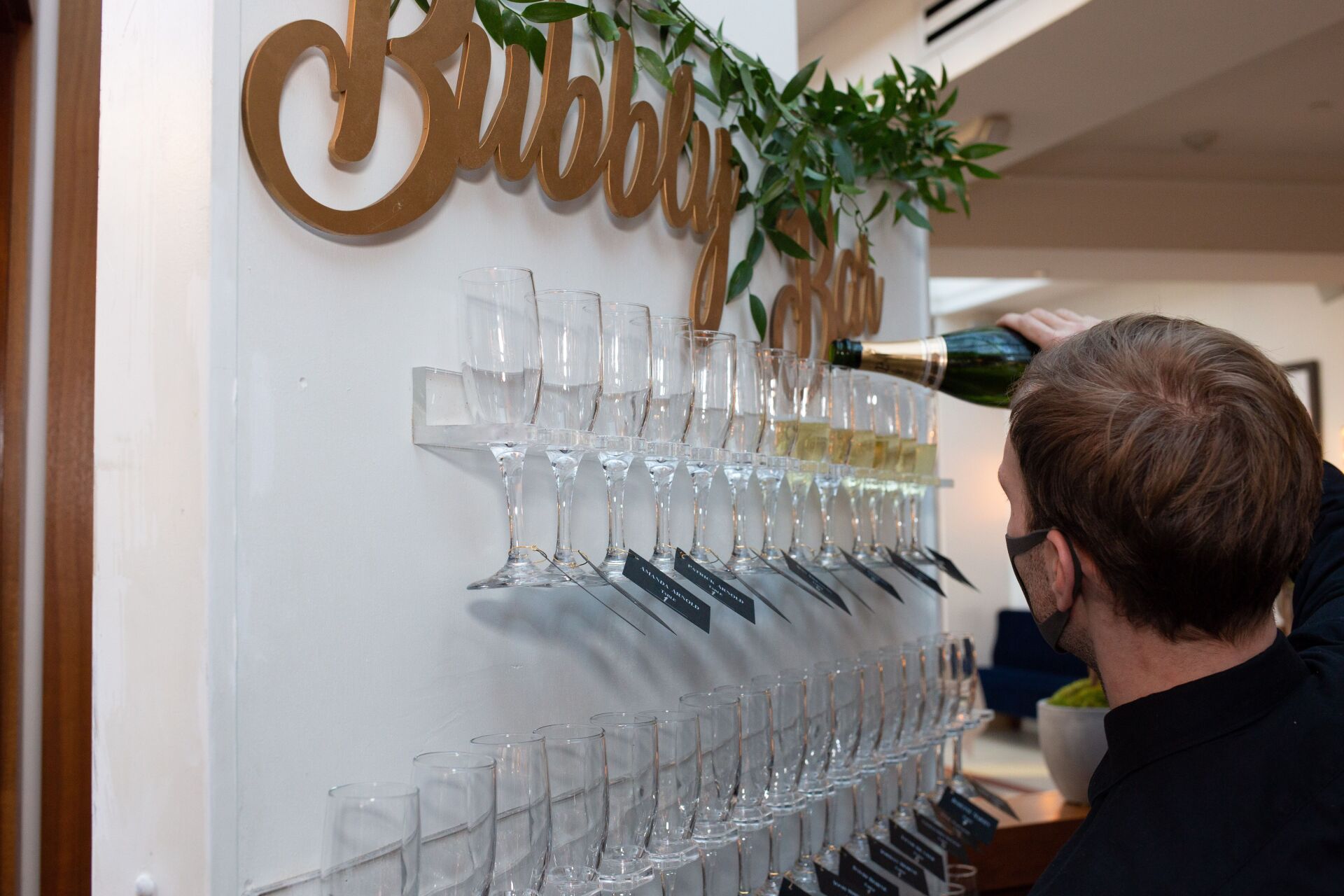A man is pouring champagne into a wall of wine glasses.