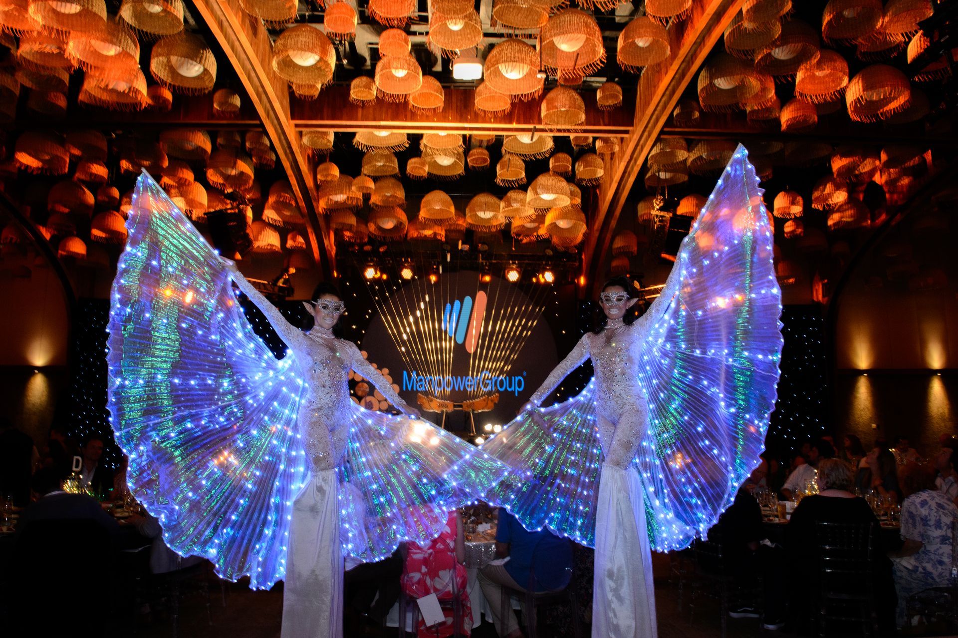 Two women wearing light up wings are standing in a room.