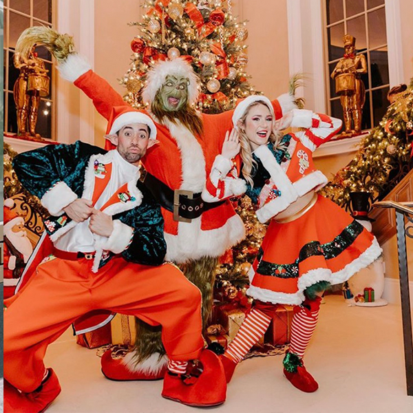 Three people dressed in christmas costumes are posing in front of a christmas tree