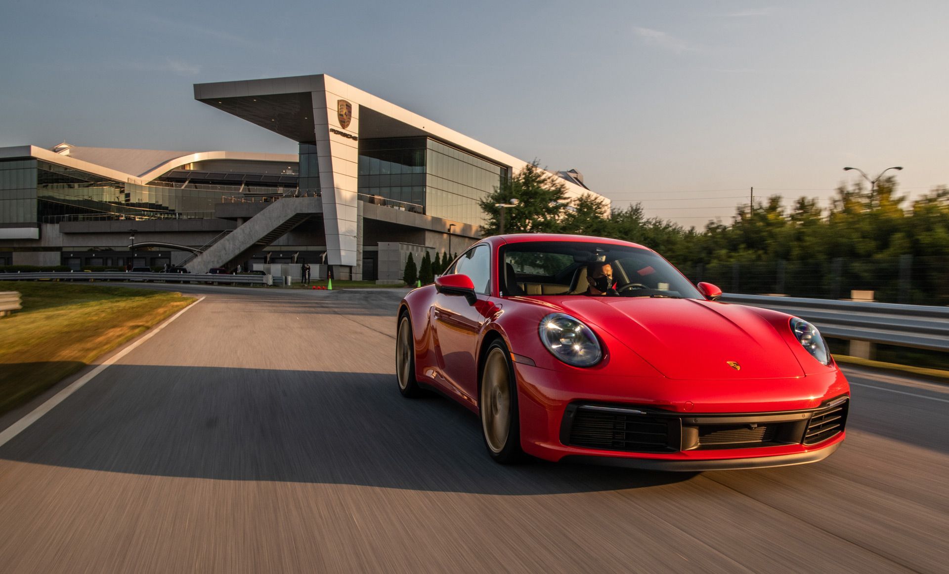 A red porsche 911 is driving down a road in front of a building.