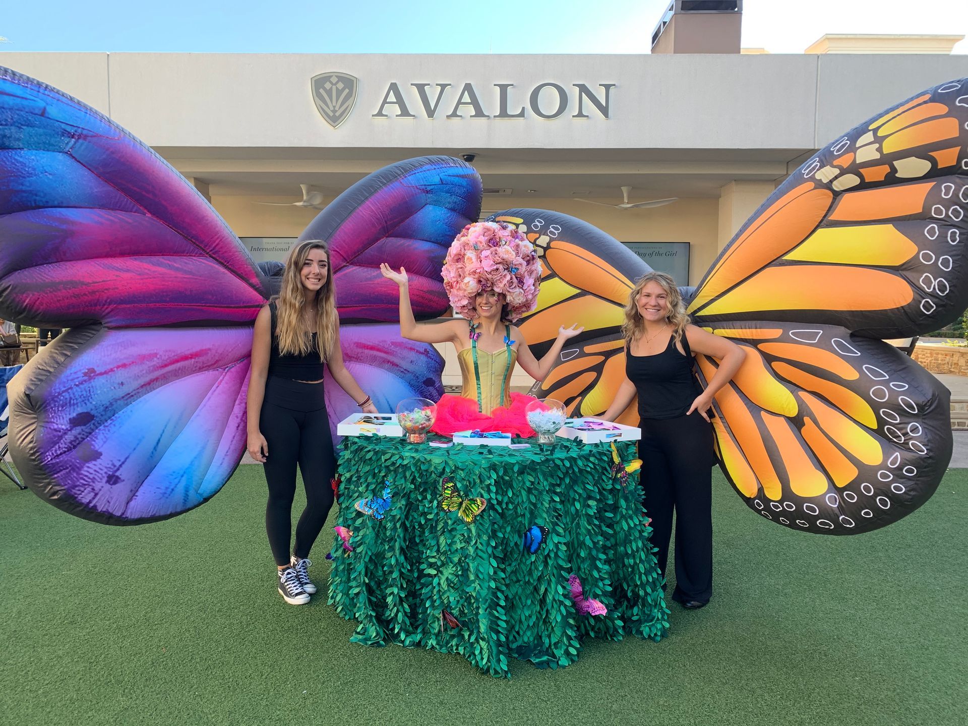 Three women dressed as butterflies are standing around a table.