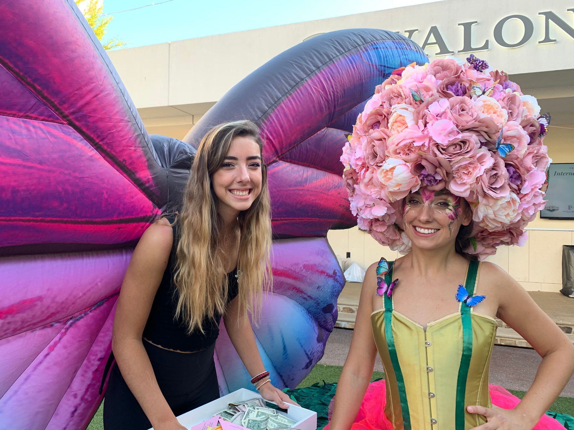 Two women are standing next to each other in front of an inflatable butterfly.