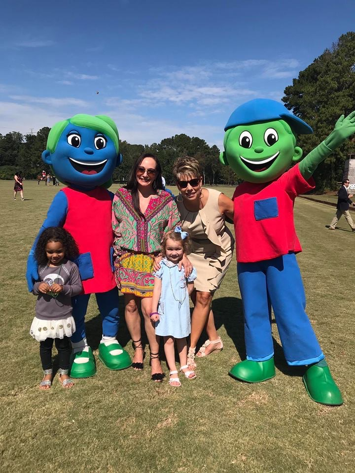 A group of people standing next to mascots in a field.