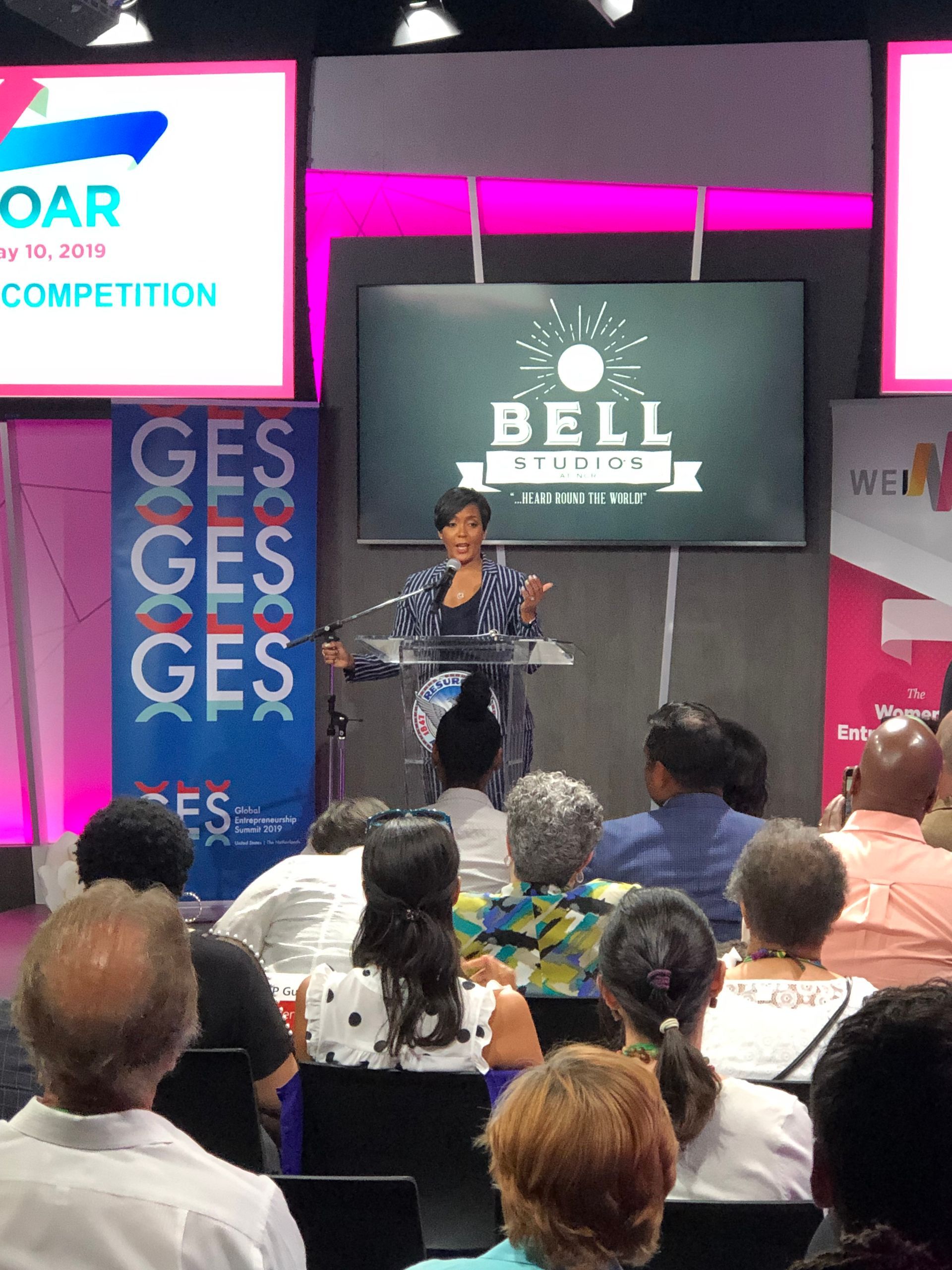 a woman is giving a speech in front of a large screen that says bell on it