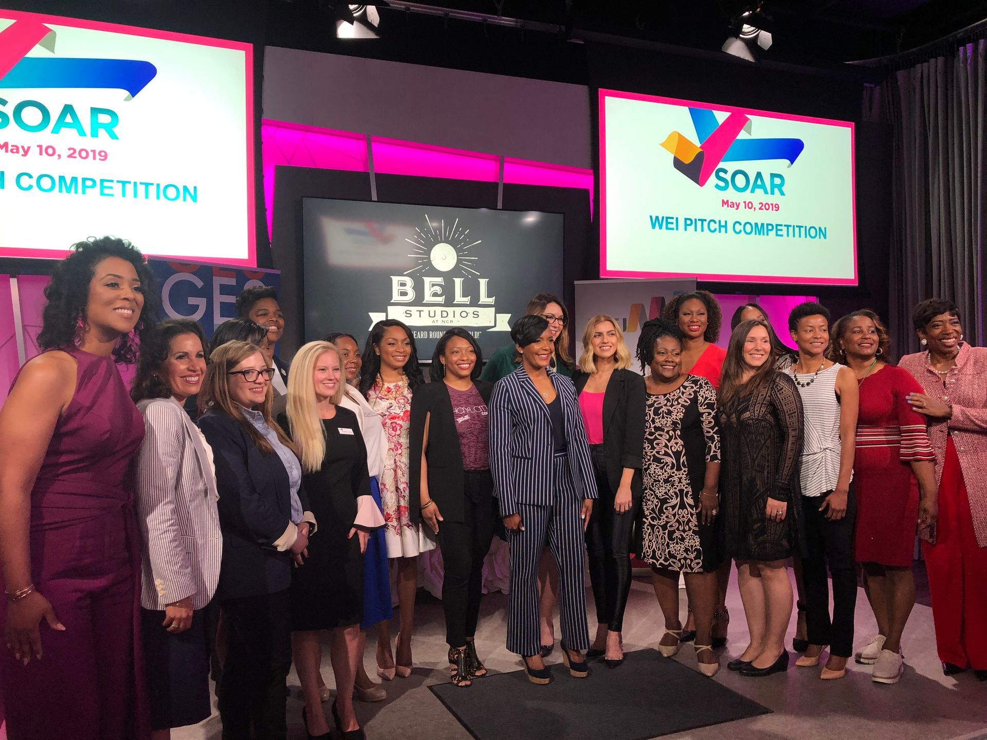 A group of women are posing for a picture in front of a large screen.