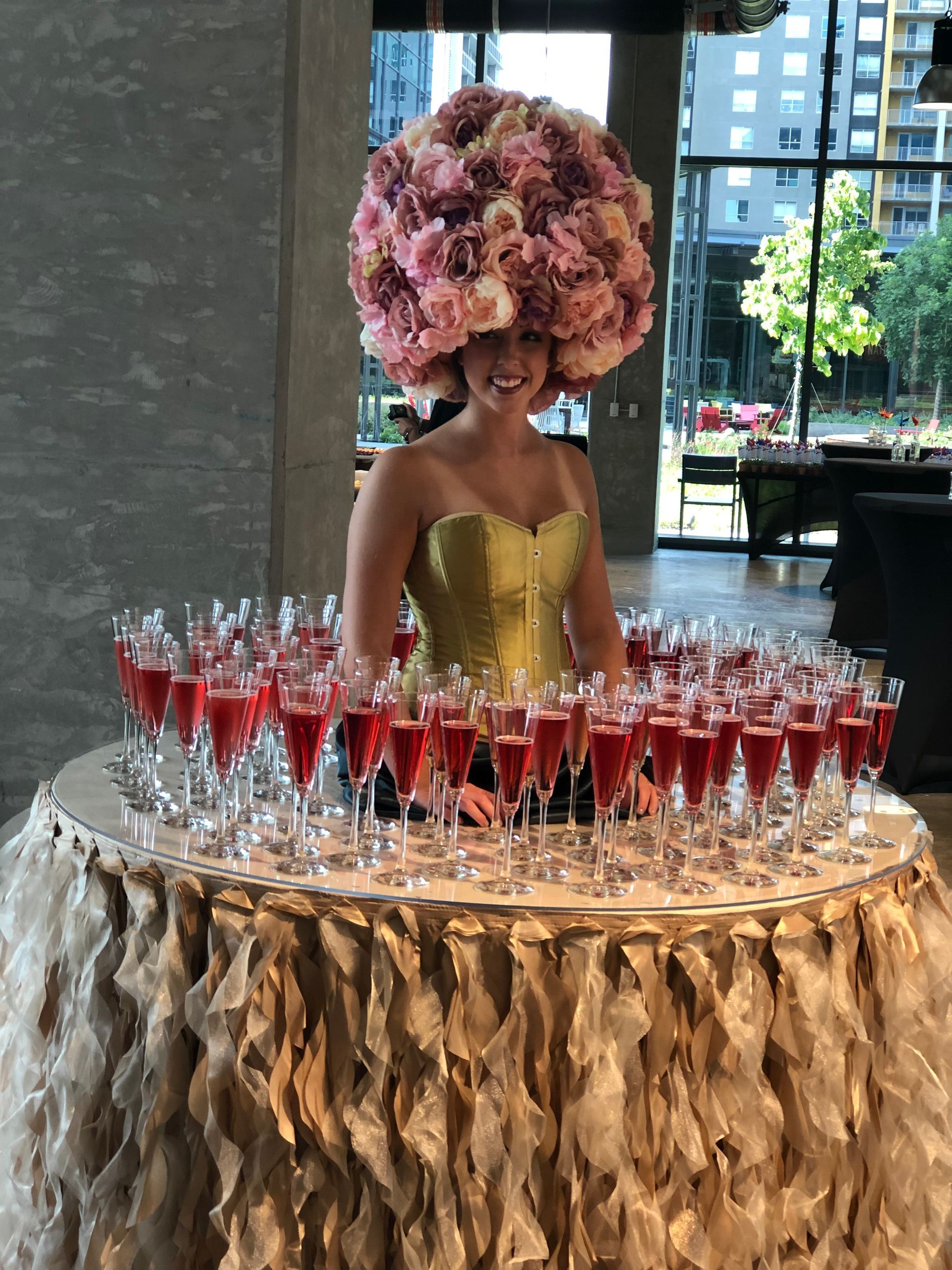 A woman in a flowered hat stands in front of a table full of wine glasses