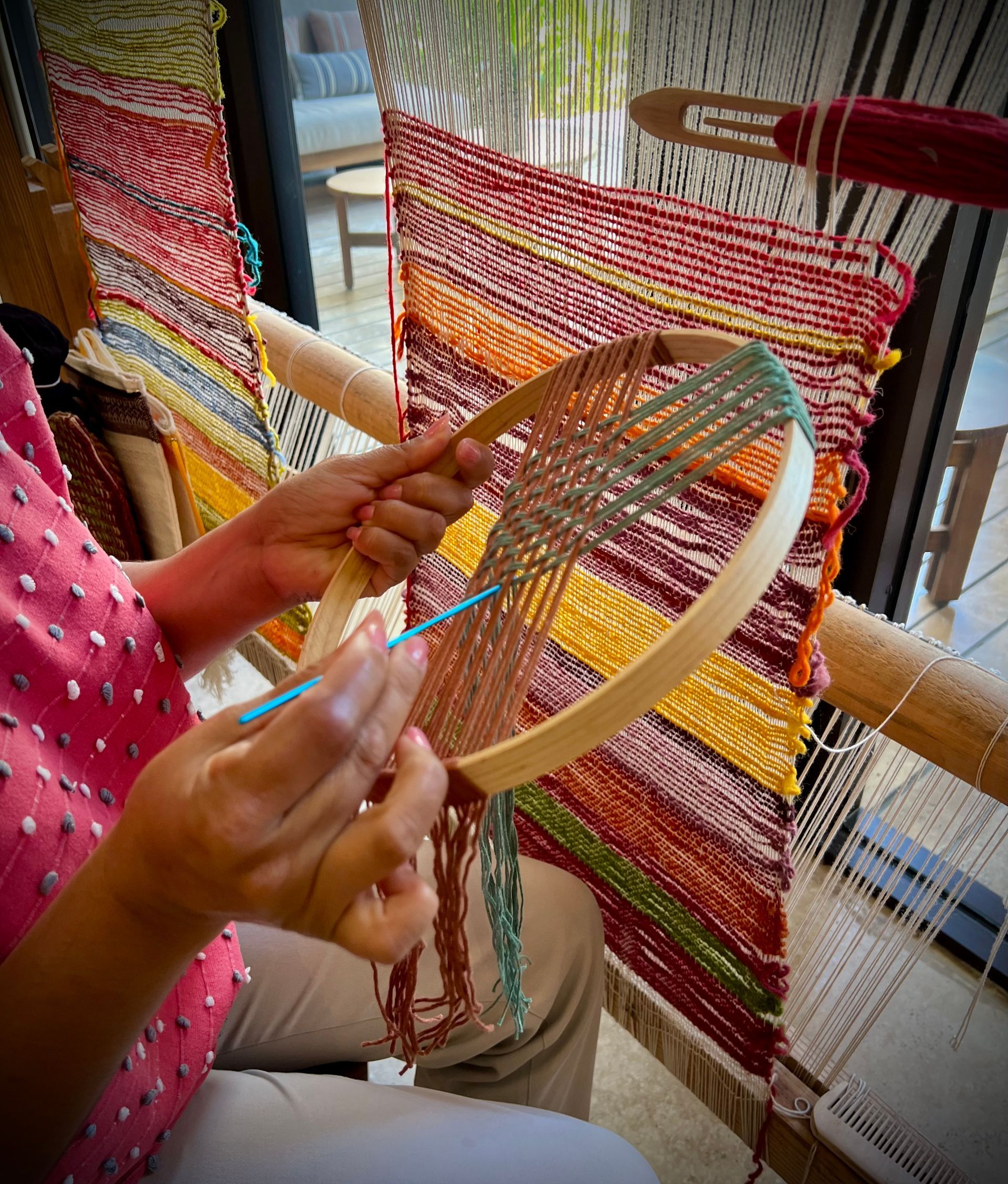 A woman is weaving a rug on a loom.