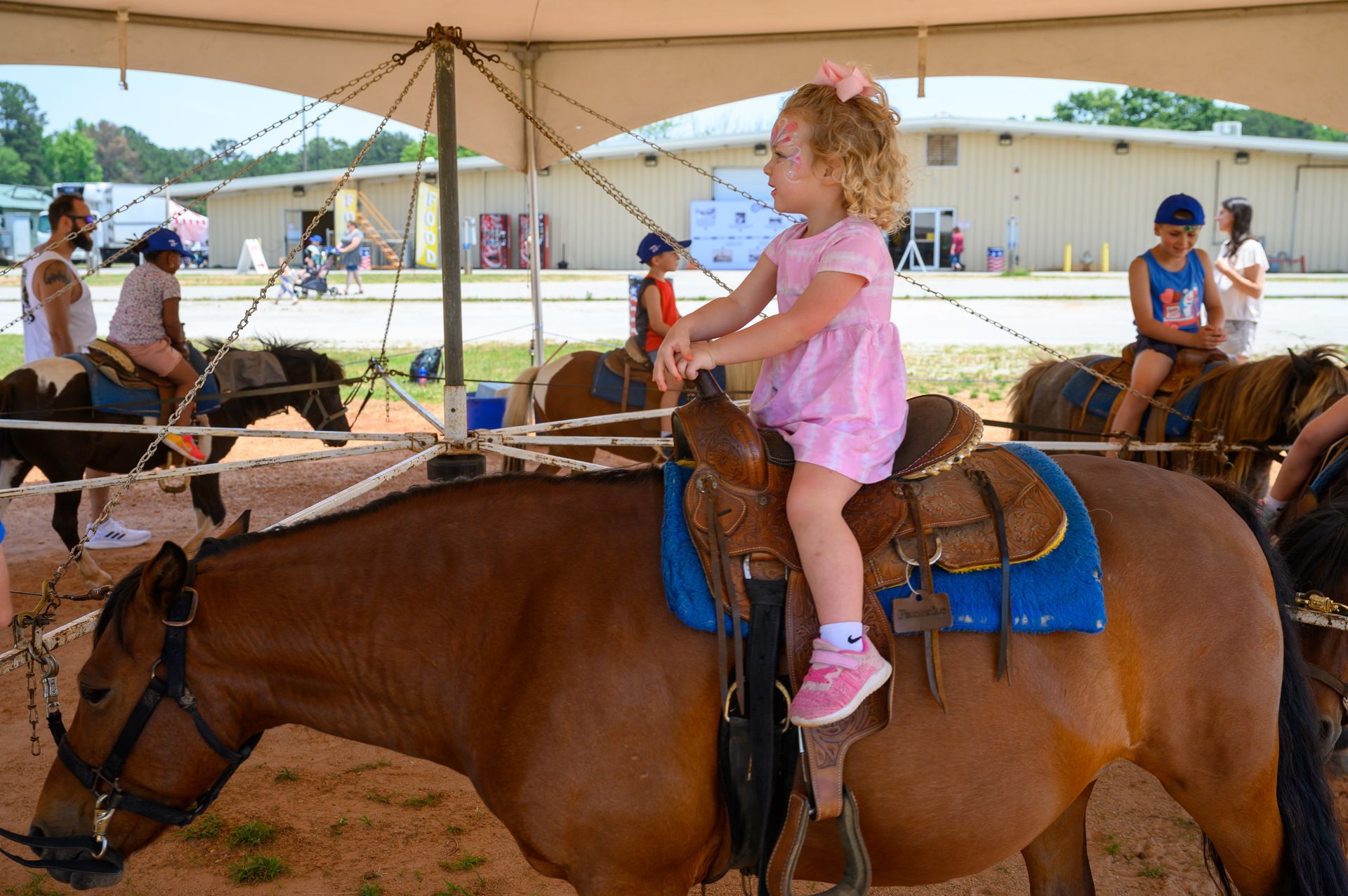 A little girl is riding a horse under a tent.