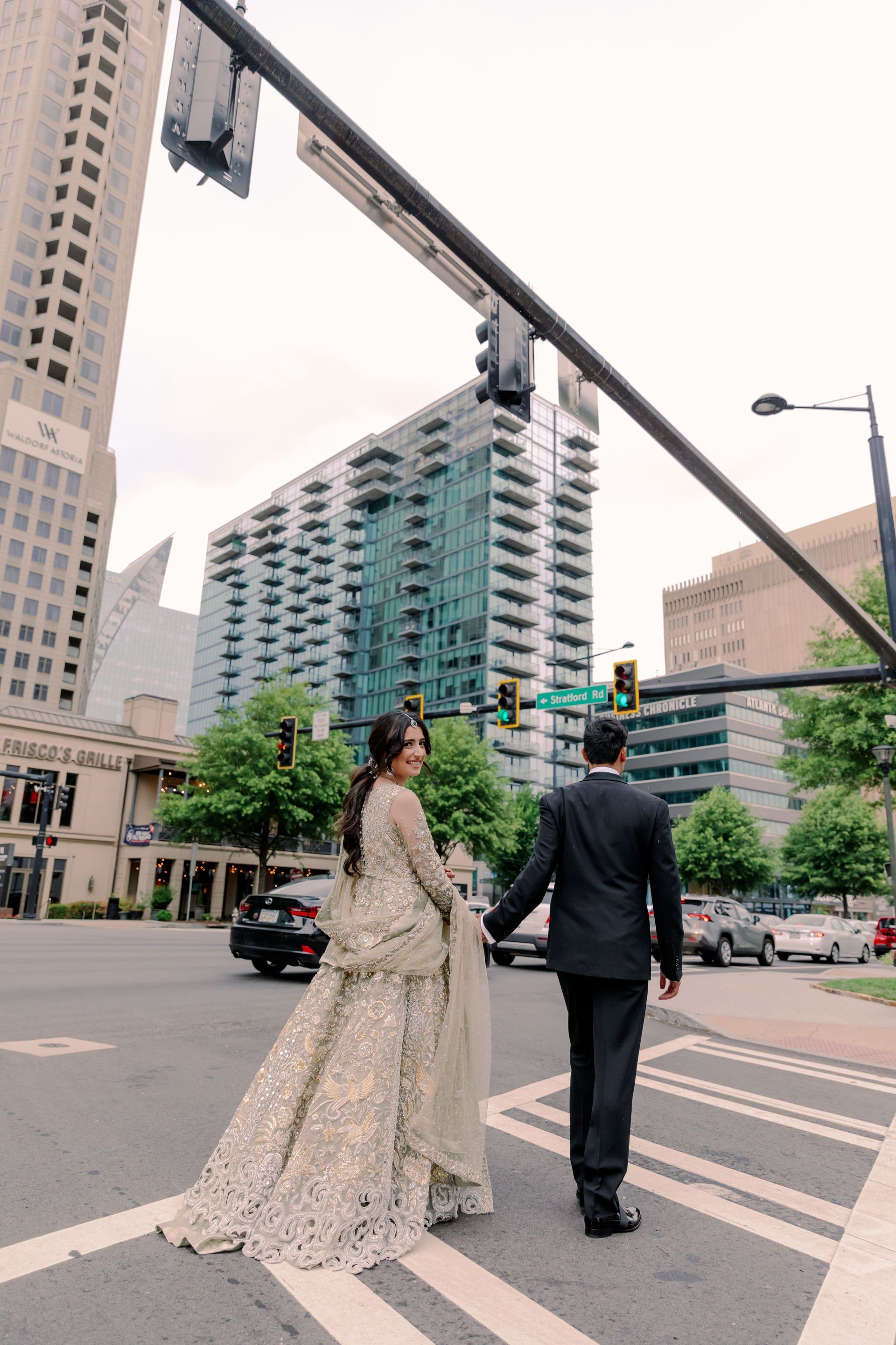 A bride and groom are walking across a city street holding hands.