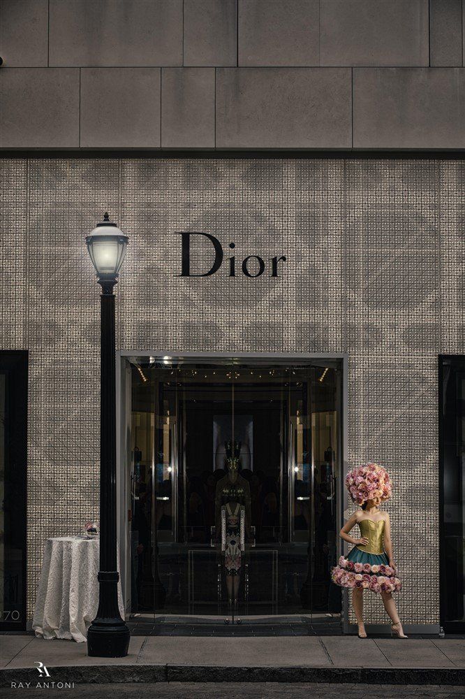A woman in a flowered hat is standing in front of a dior store.