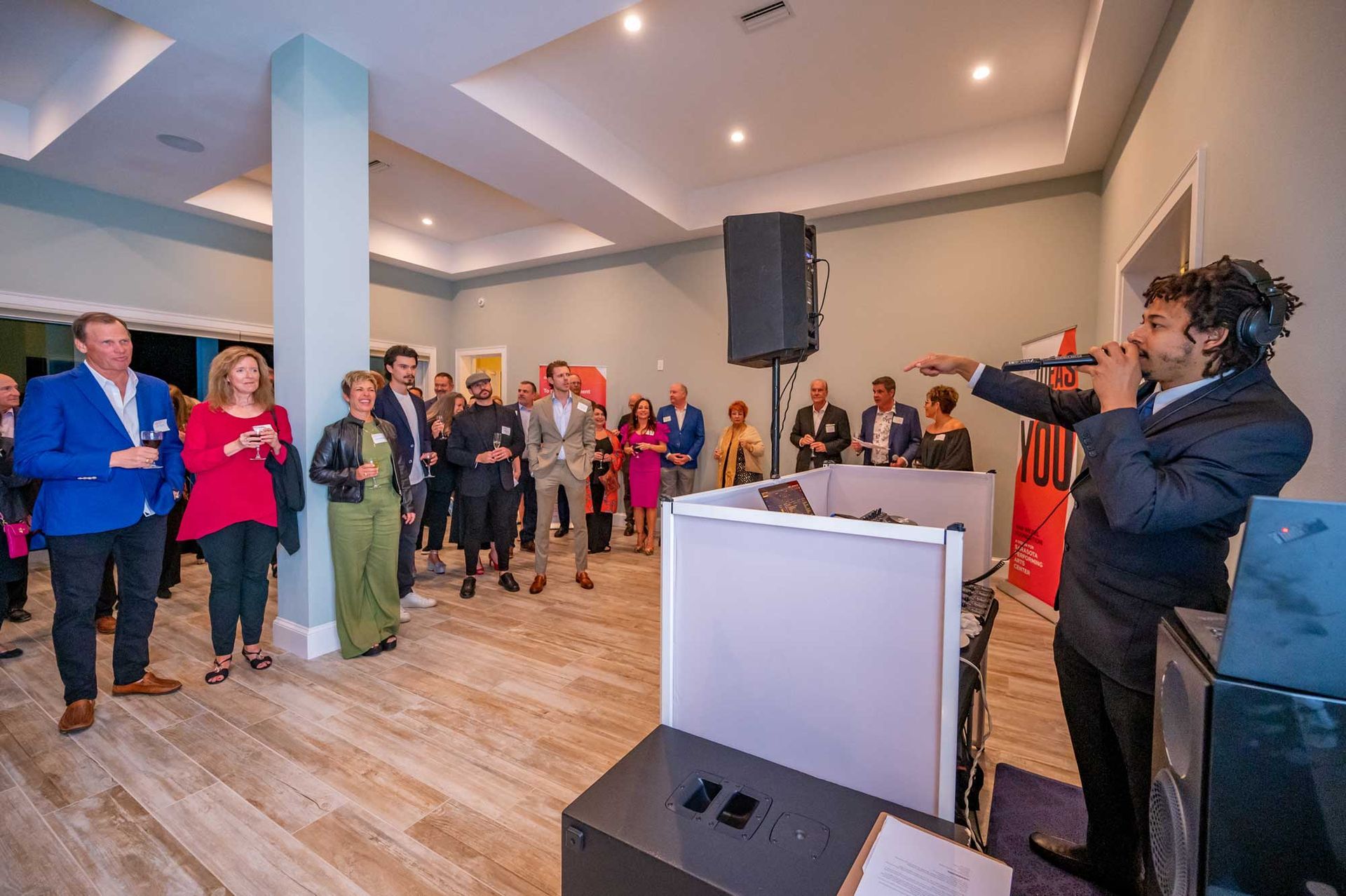 A man is singing into a microphone in front of a crowd of people at a party.