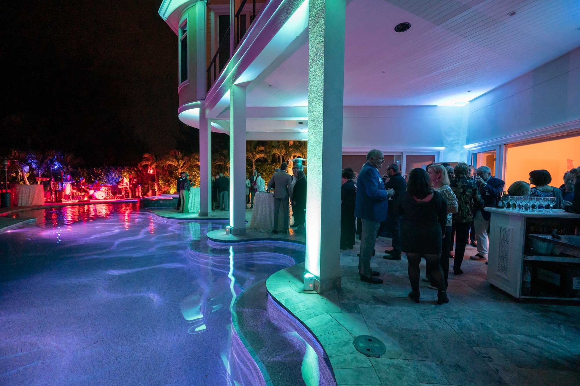 A group of people are standing around a swimming pool at night.