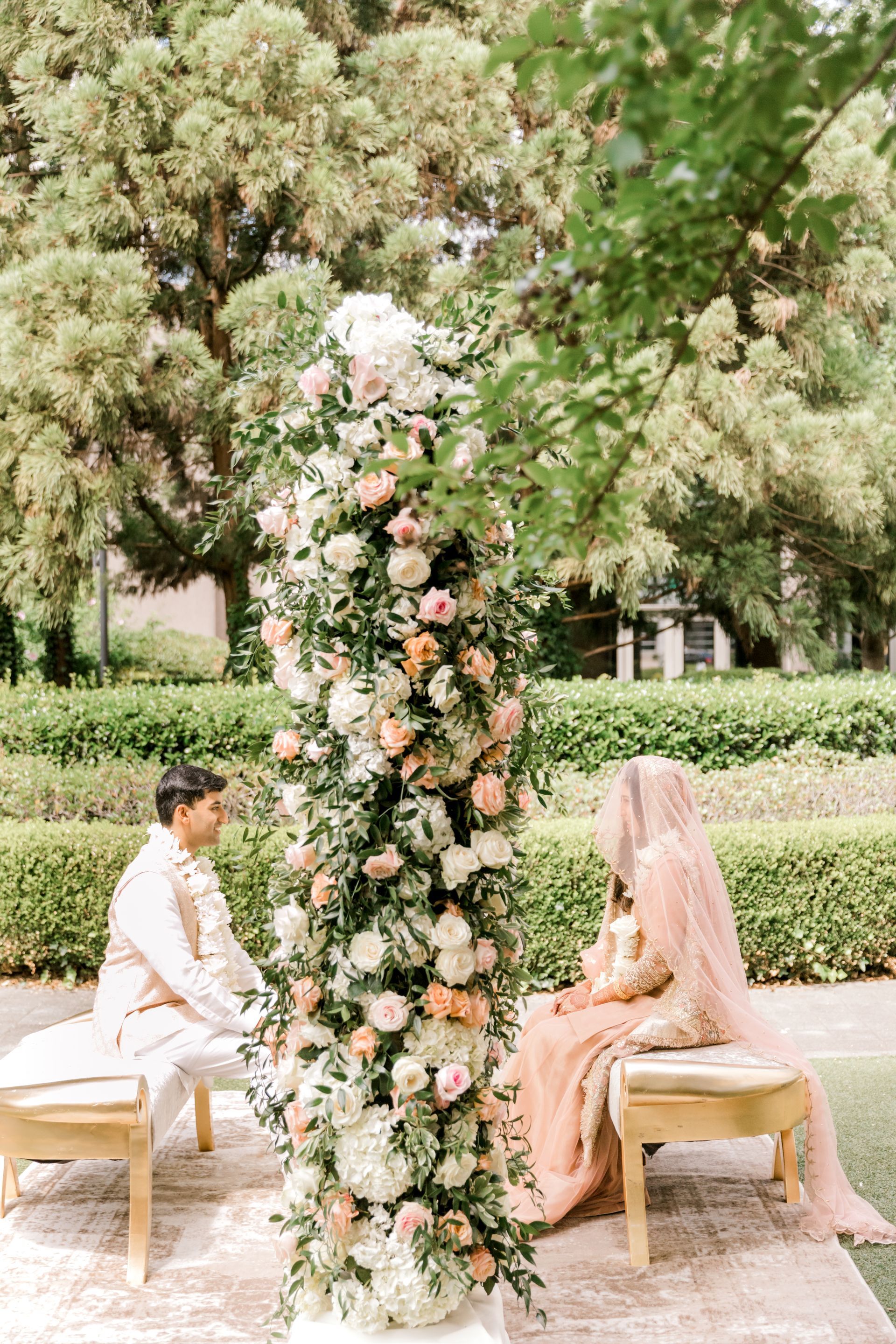 A bride and groom are sitting under a floral arch at their wedding ceremony.