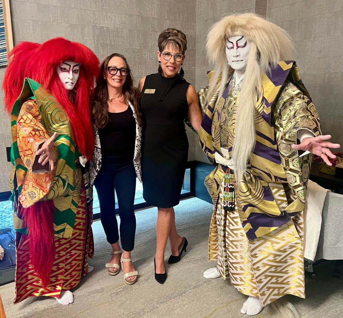 Two women pose with two Kabuki performers in ornate costumes.