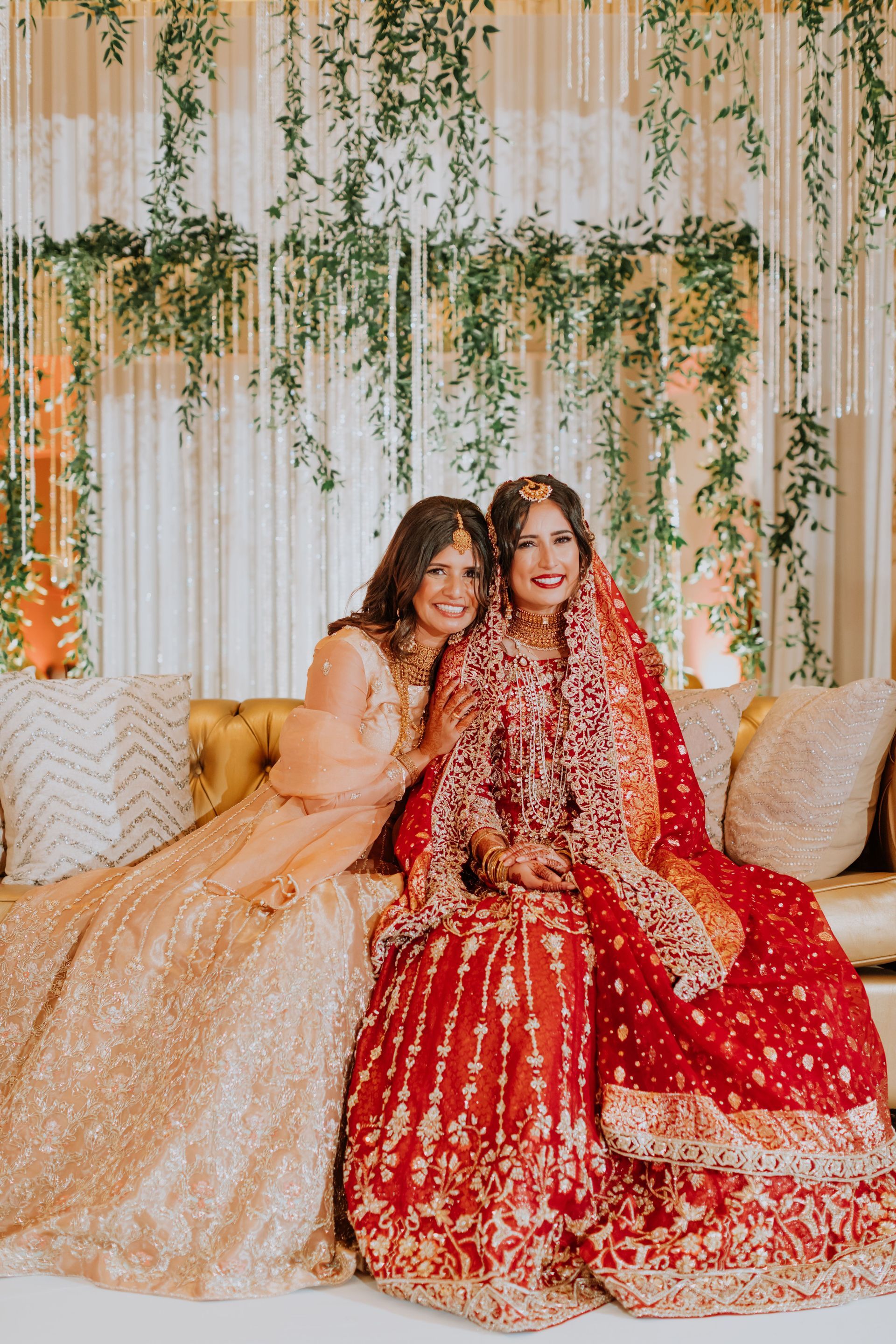 Two women in wedding dresses are sitting on a couch.