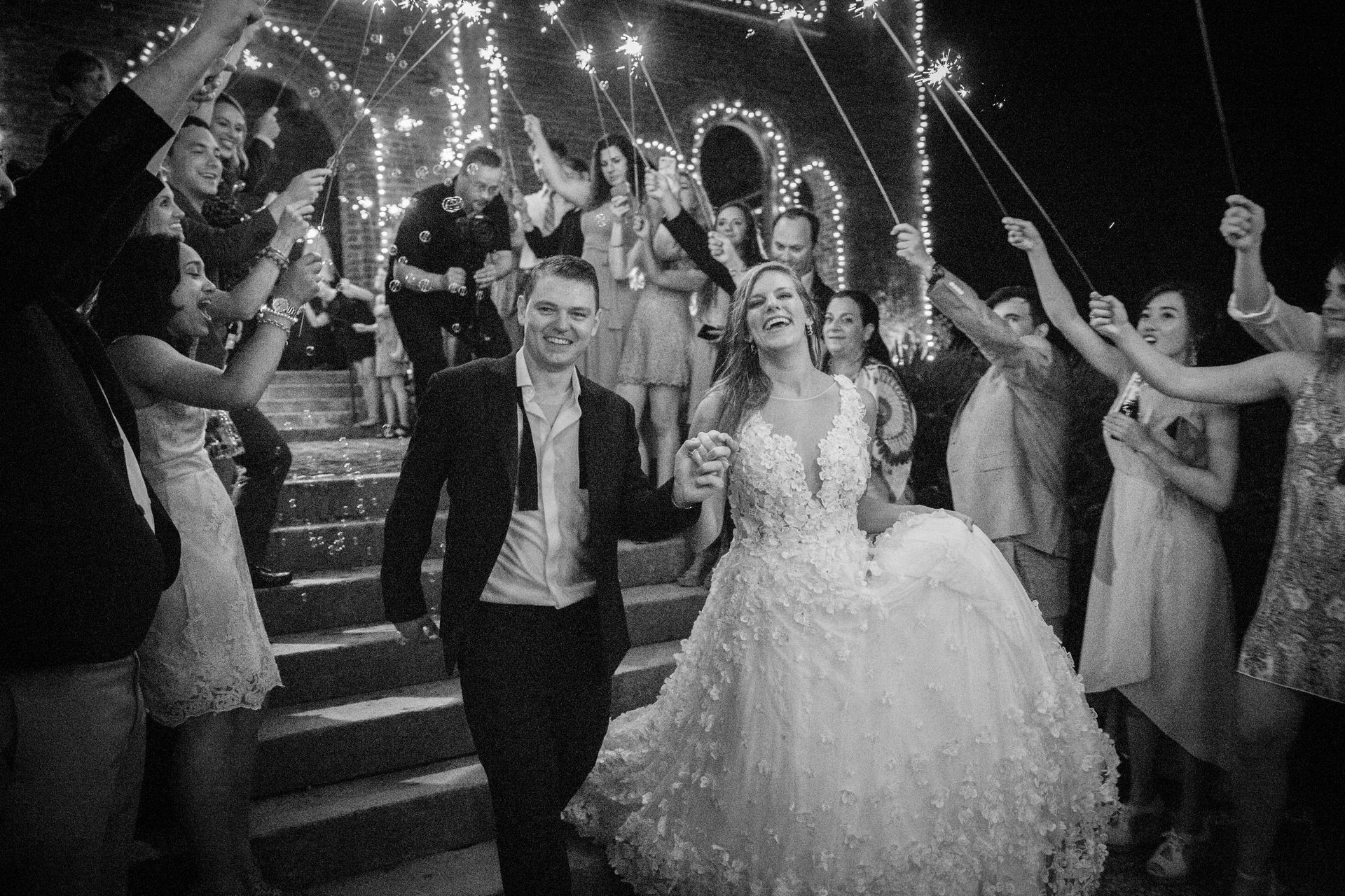 A black and white photo of a bride and groom walking through a tunnel of sparklers.