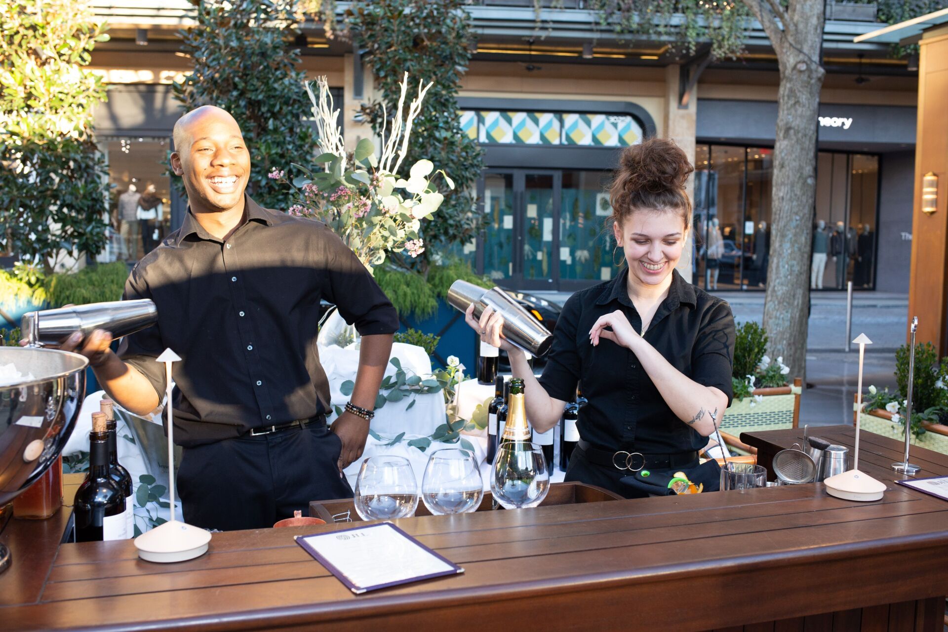 A man and a woman are standing at a bar making drinks.