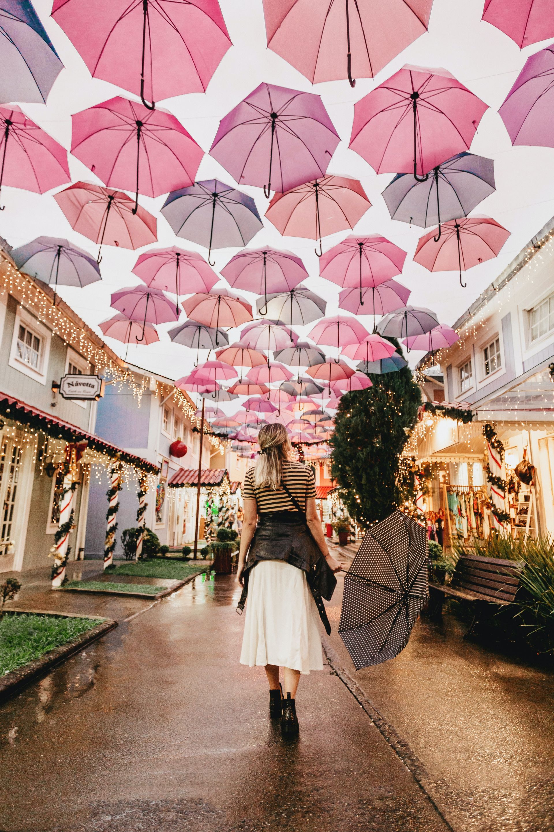 a woman is walking down a street with umbrellas hanging from the ceiling .