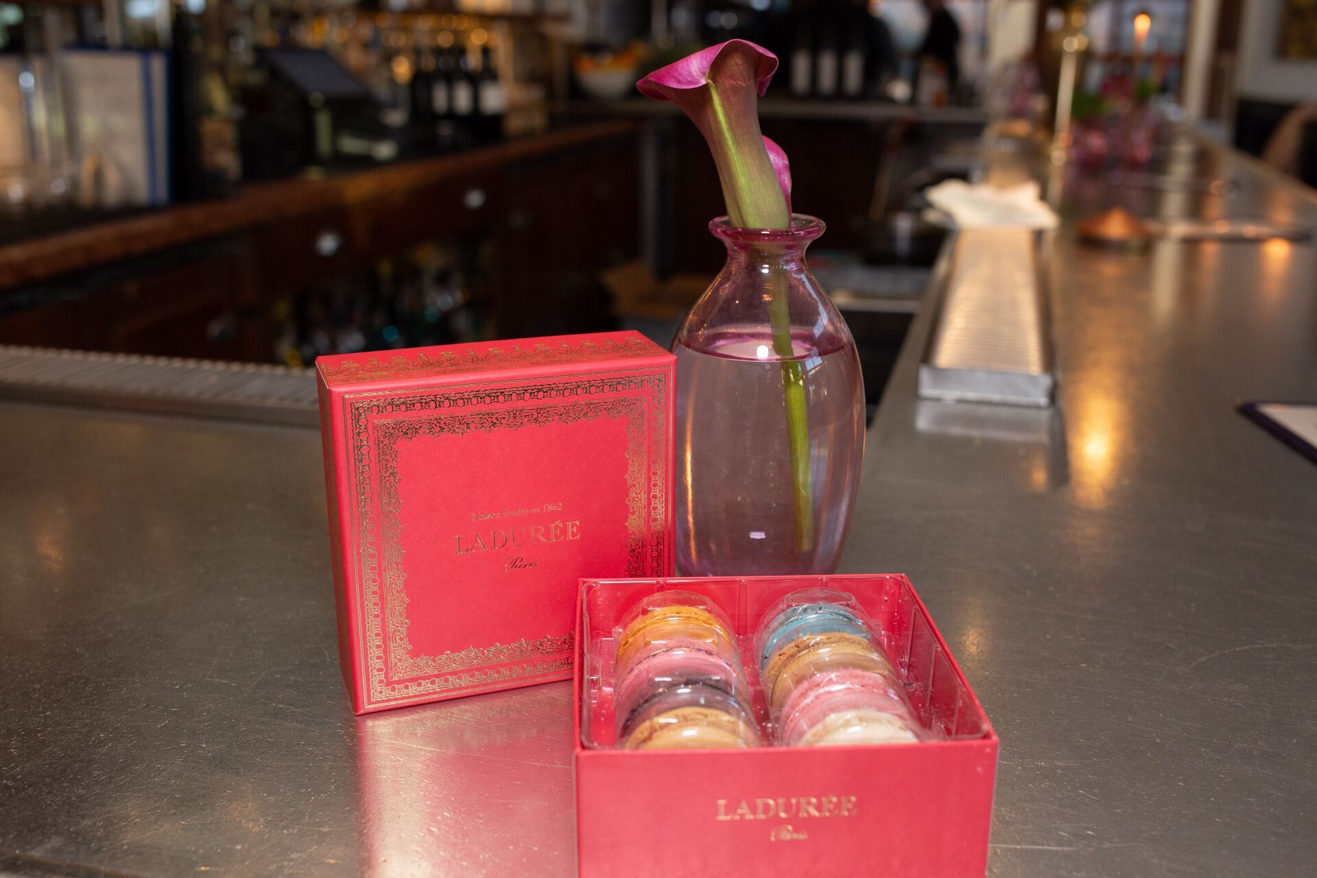 A box of macarons is sitting on a counter next to a vase of flowers.