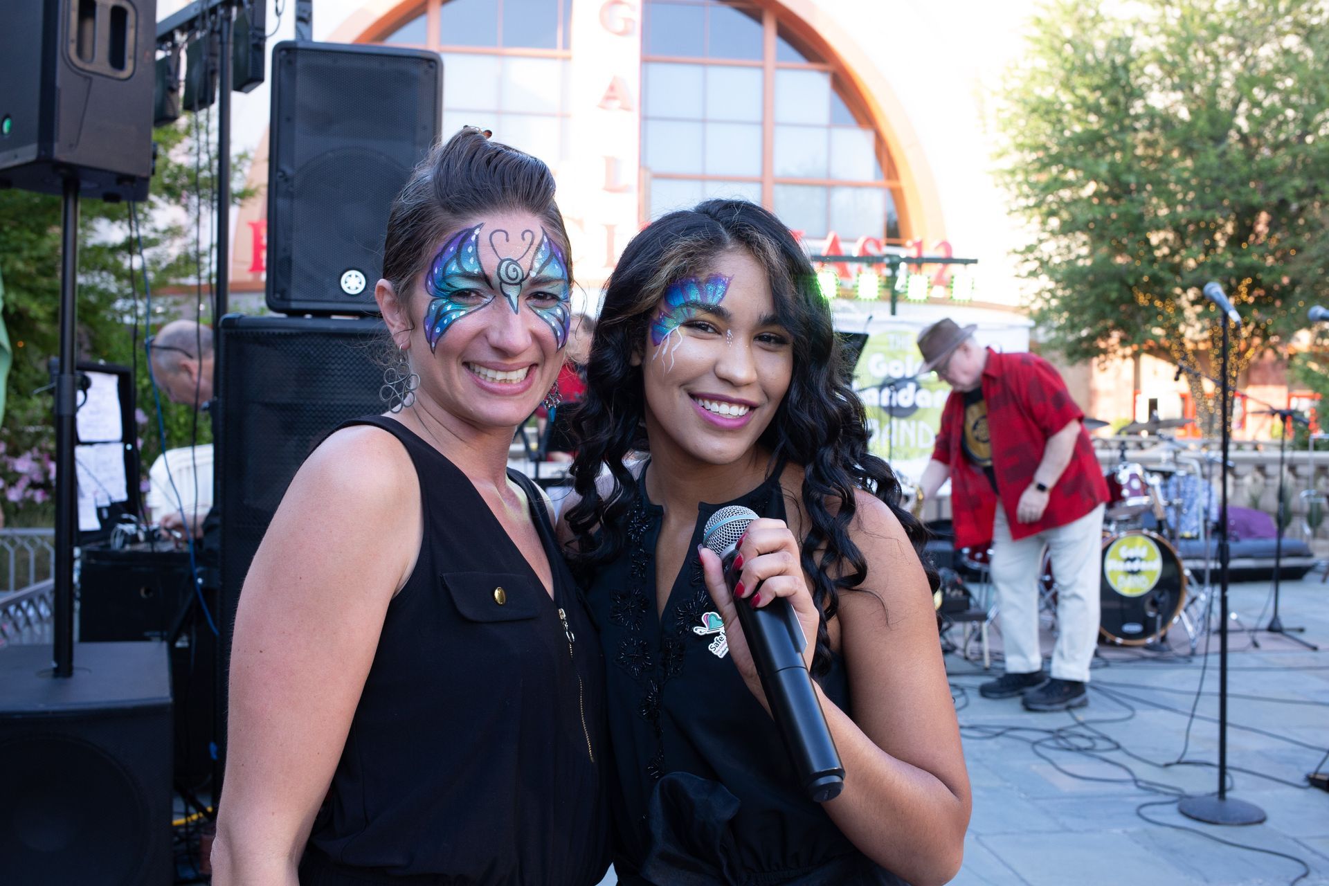 Two women with face paint are standing next to each other holding microphones.