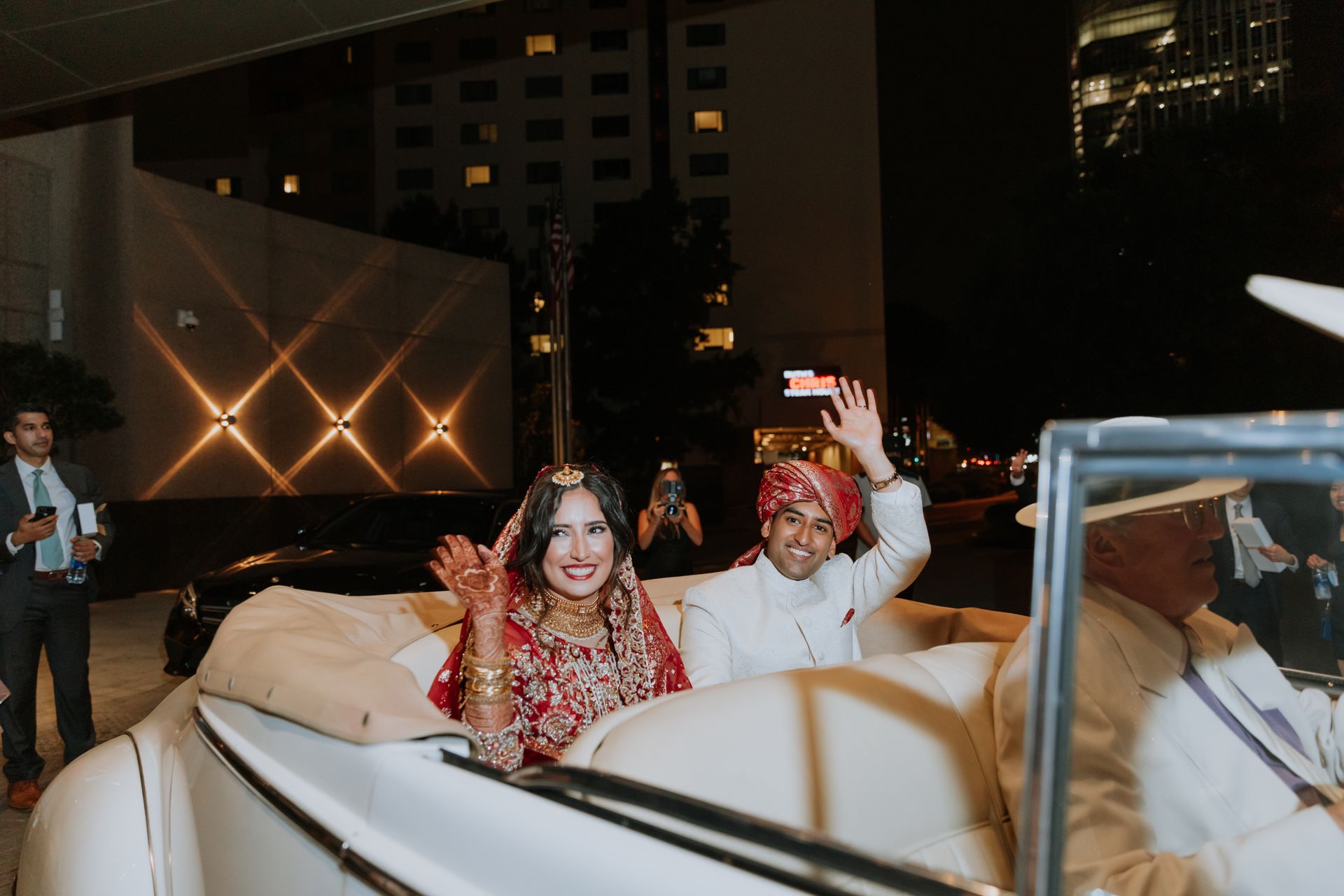 A bride and groom are riding in the back of a car.