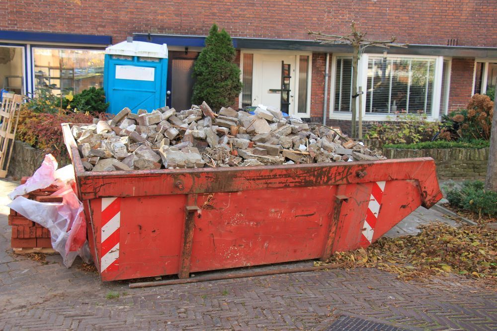 A Red Dumpster Filled with Bricks Is in Front of A Brick House — Hyper Cut & Drill in Gosford, NSW