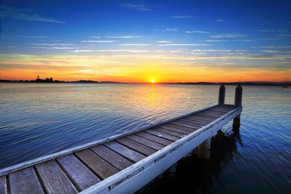 A Wooden Dock Overlooking a Body of Water at Sunset — Hyper Cut & Drill in Lake Macquarie, NSW