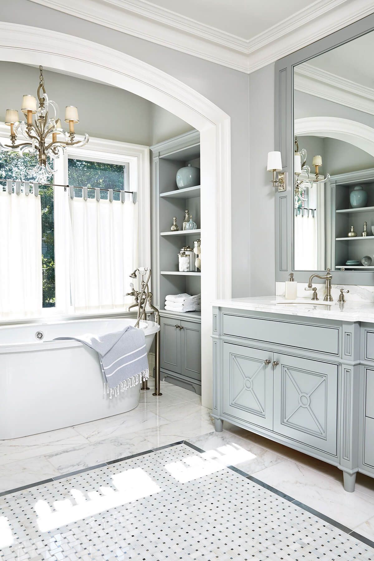 Elegant gray and white bathroom with a tub, vanity, and built-in shelving.