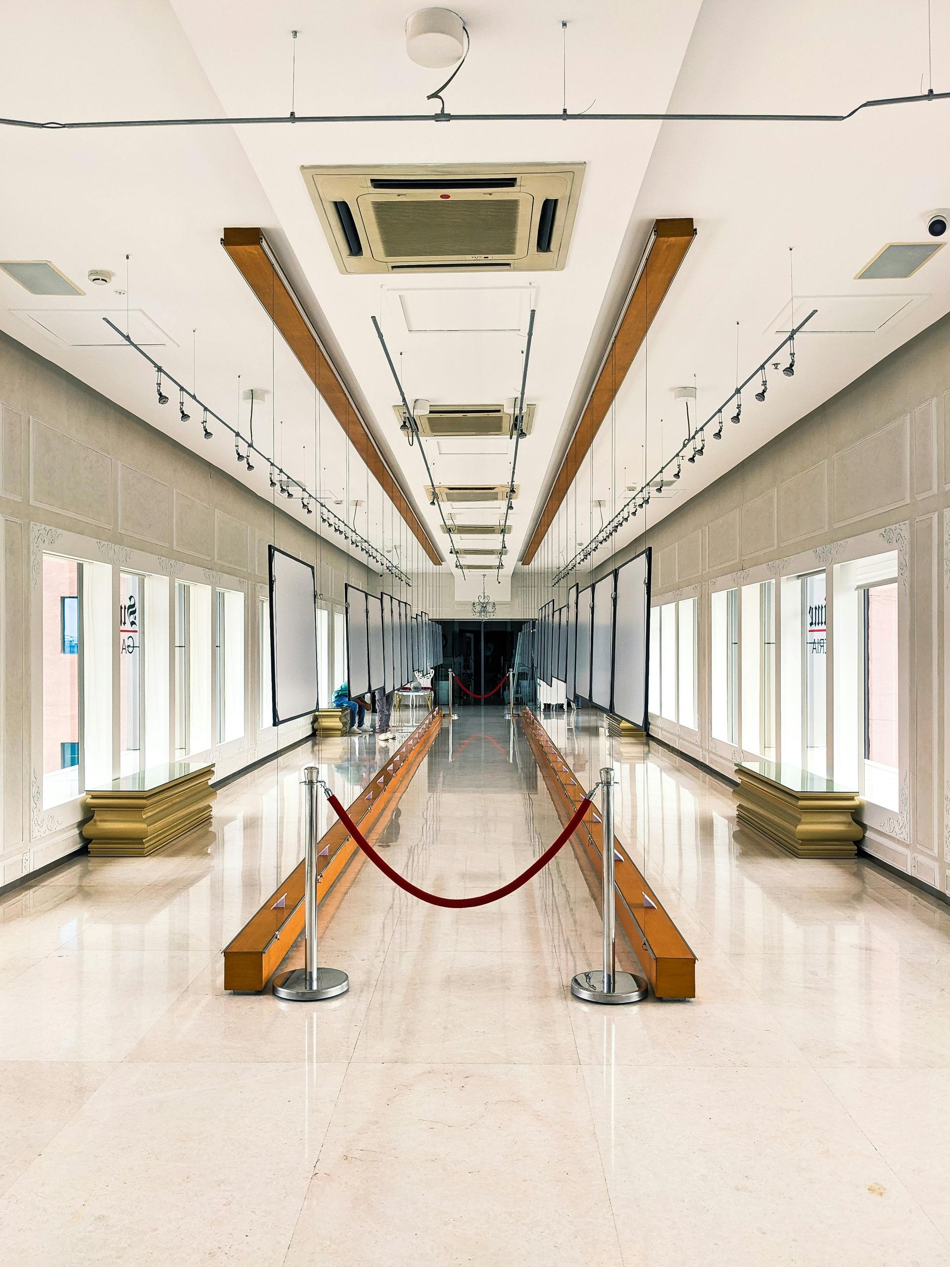 Long, white hallway with display cases, rope barrier, and air conditioning units.