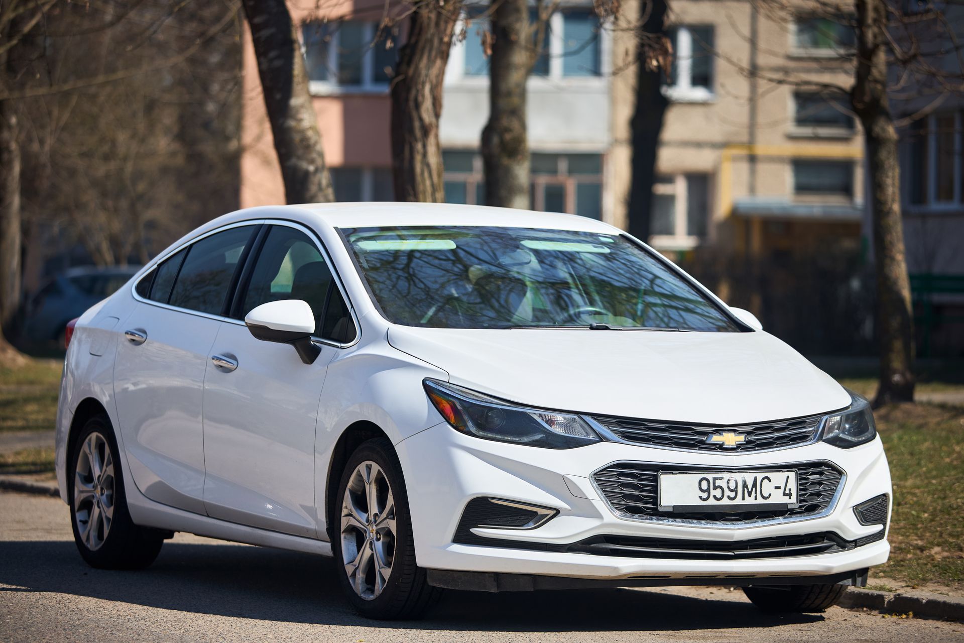 White sedan parked outdoors in front of buildings and trees