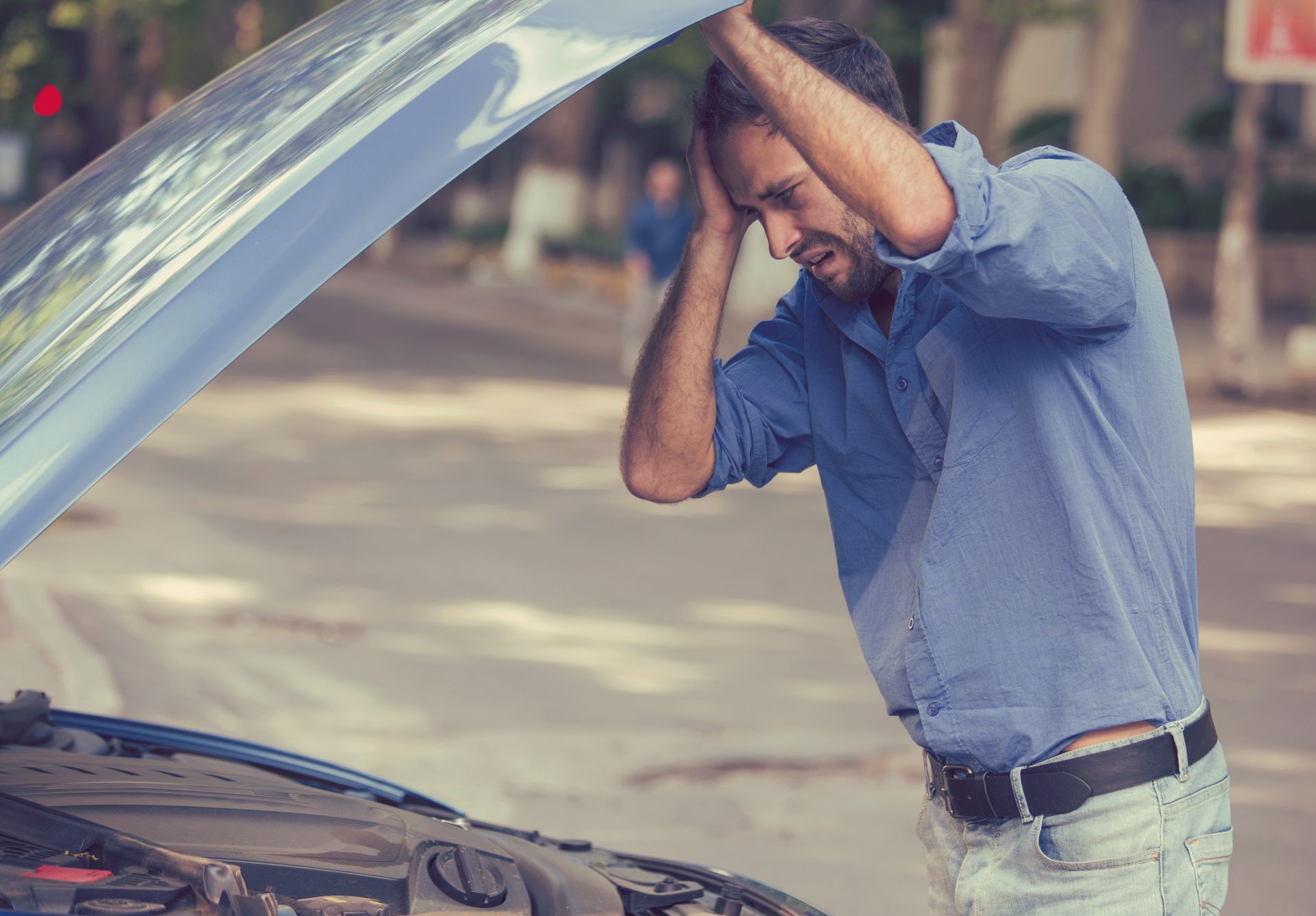 Man in a blue shirt with raised hood prop, inspecting a car engine with the hood open