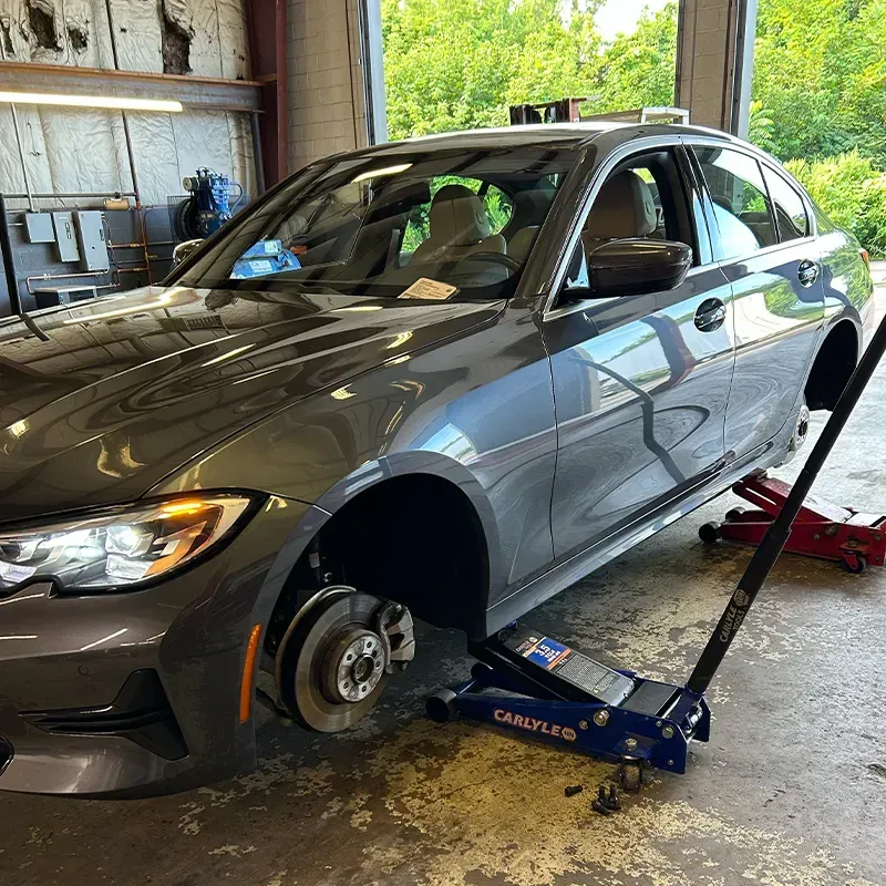 Gray sedan on a jack in a garage, front wheel removed for repair