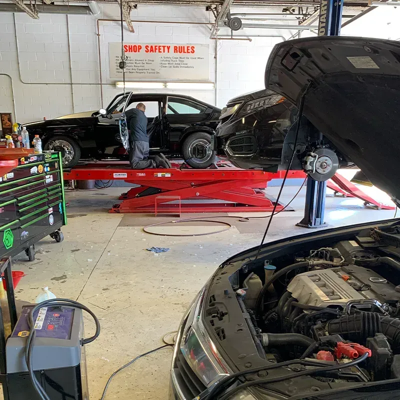 Cars on hydraulic lifts inside an auto repair shop, with a mechanic working near the center lift.