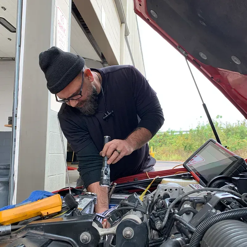 Mechanic working under an open car hood with a wrench in an outdoor garage area